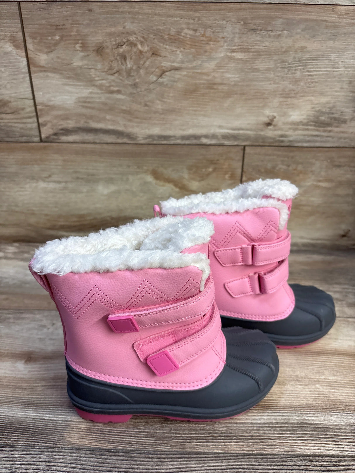 Side view of Cat & Jack Denver toddler winter boots in pink showing white faux-fur lining, dual hook-and-loop straps, and black rubber toe on wood background