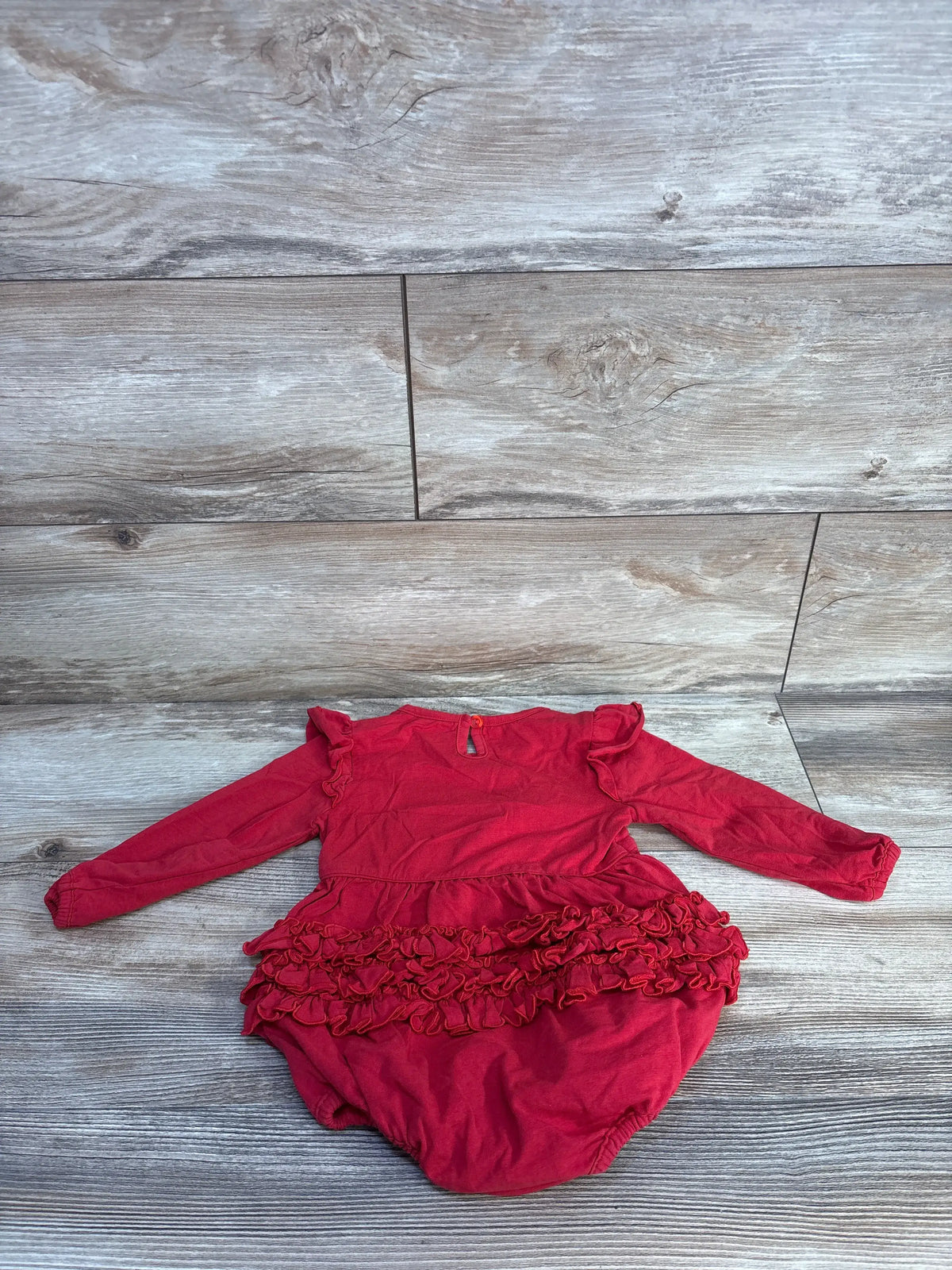 Front view of Ruffle Butts red long sleeve ruffle bubble romper showcasing layered ruffle details, laid flat on a gray wood floor