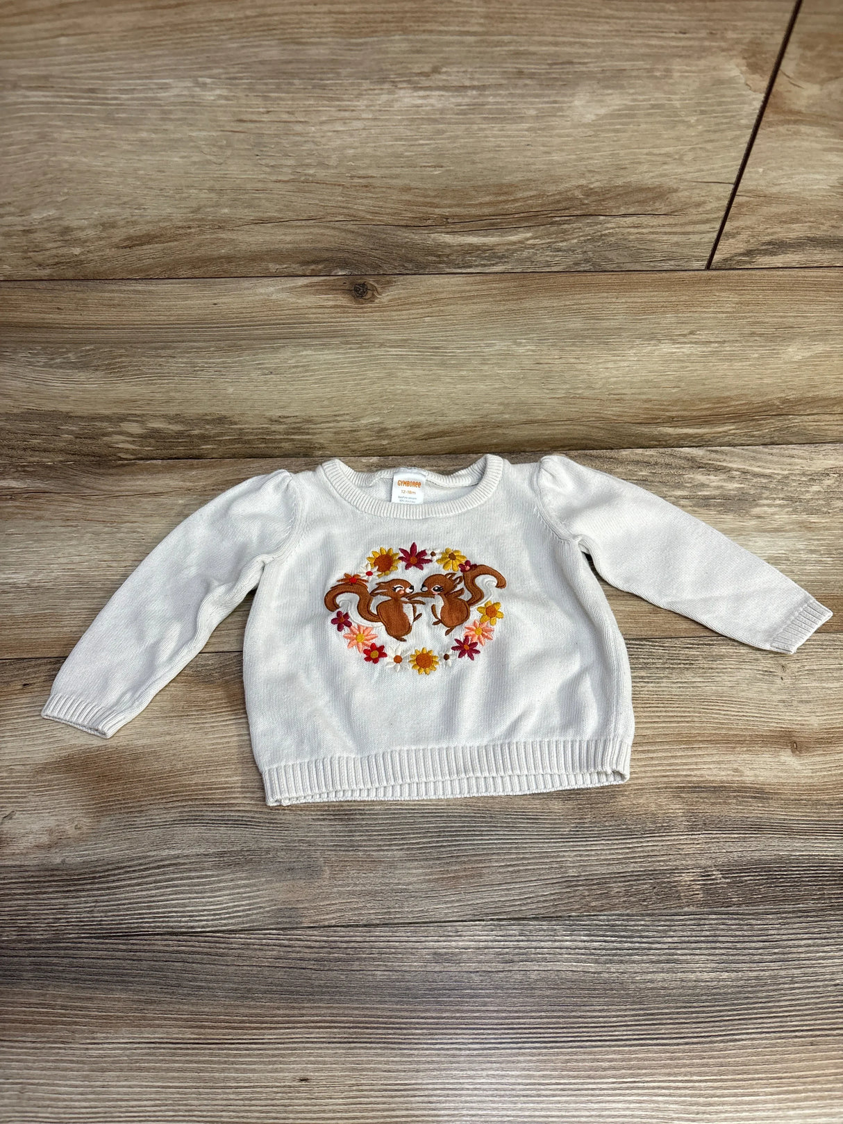White baby sweater with embroidered squirrels and flowers on wood background