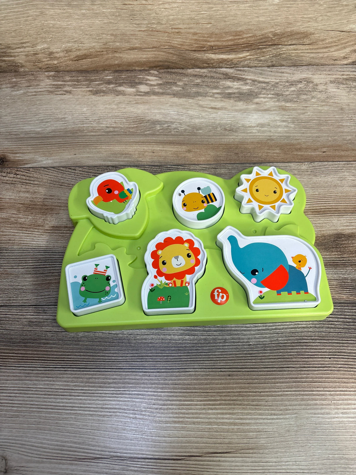 Fisher-Price green animal puzzle toy with lion, elephant, sun, bee, frog, and bird on wood table