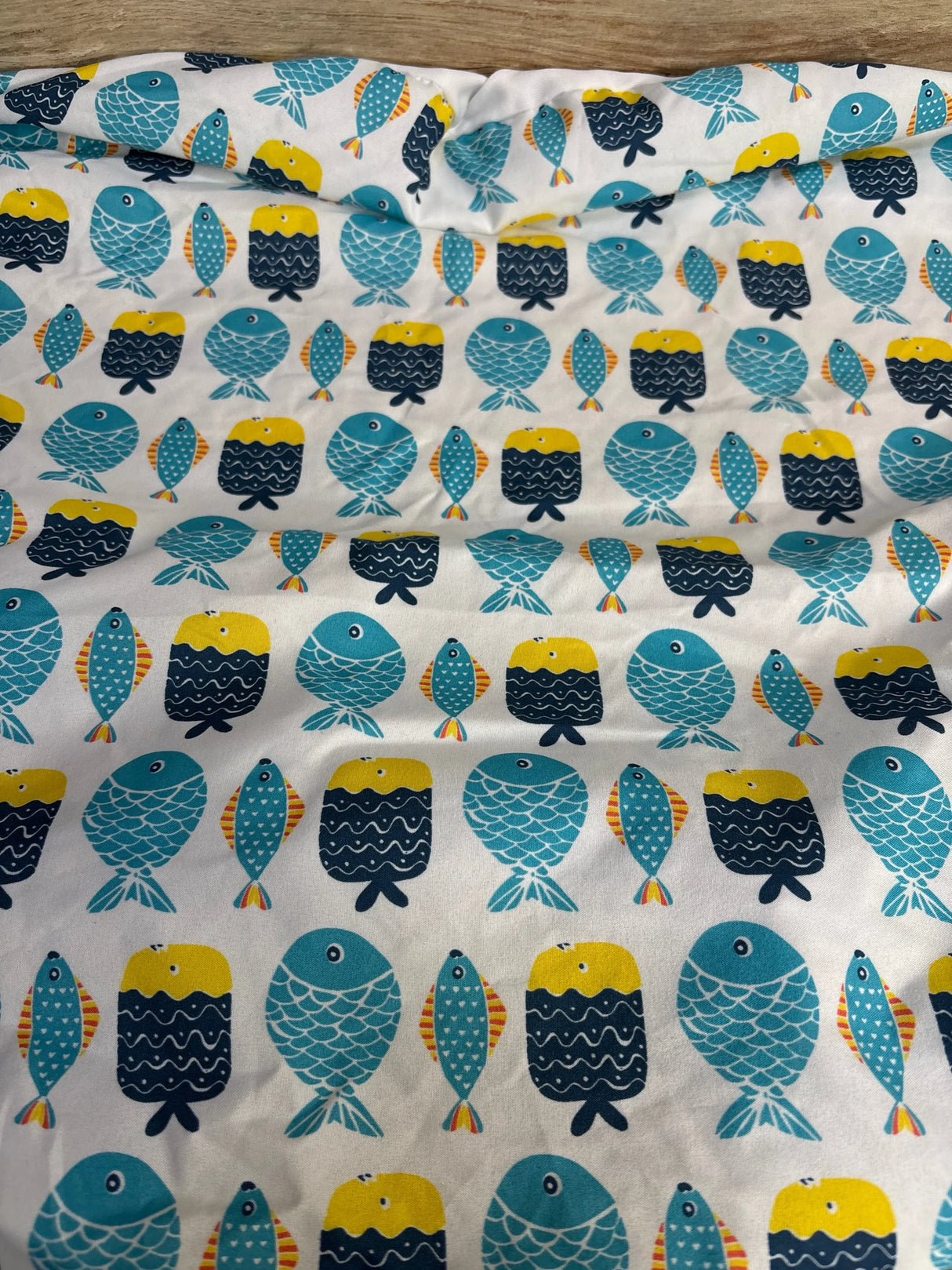 White fabric with colorful cartoon fish pattern in blue, yellow, and orange accents