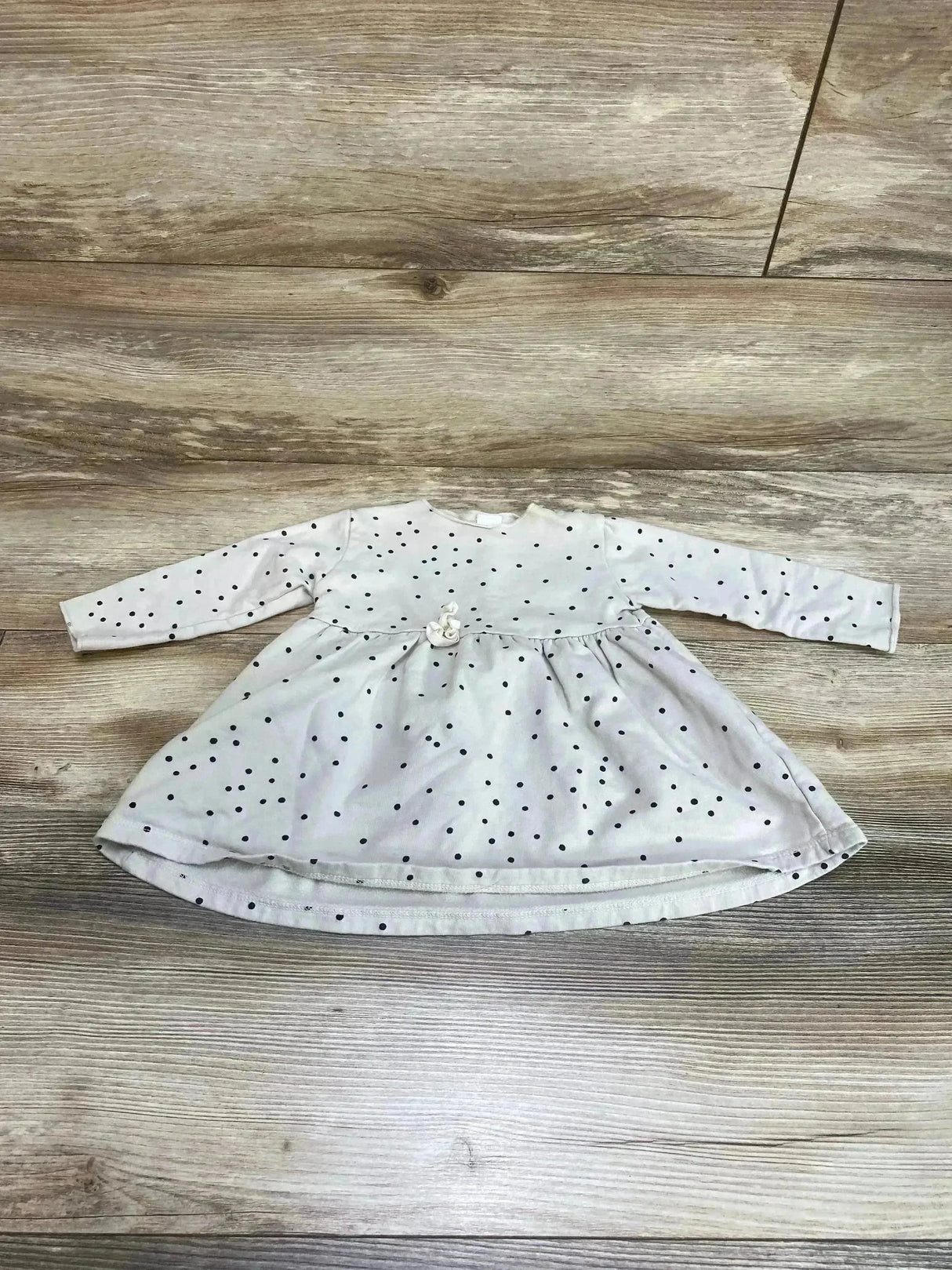 Flat lay of beige long-sleeve baby dress with black polka dots and gathered waist flower, size 6-12 months on wood floor
