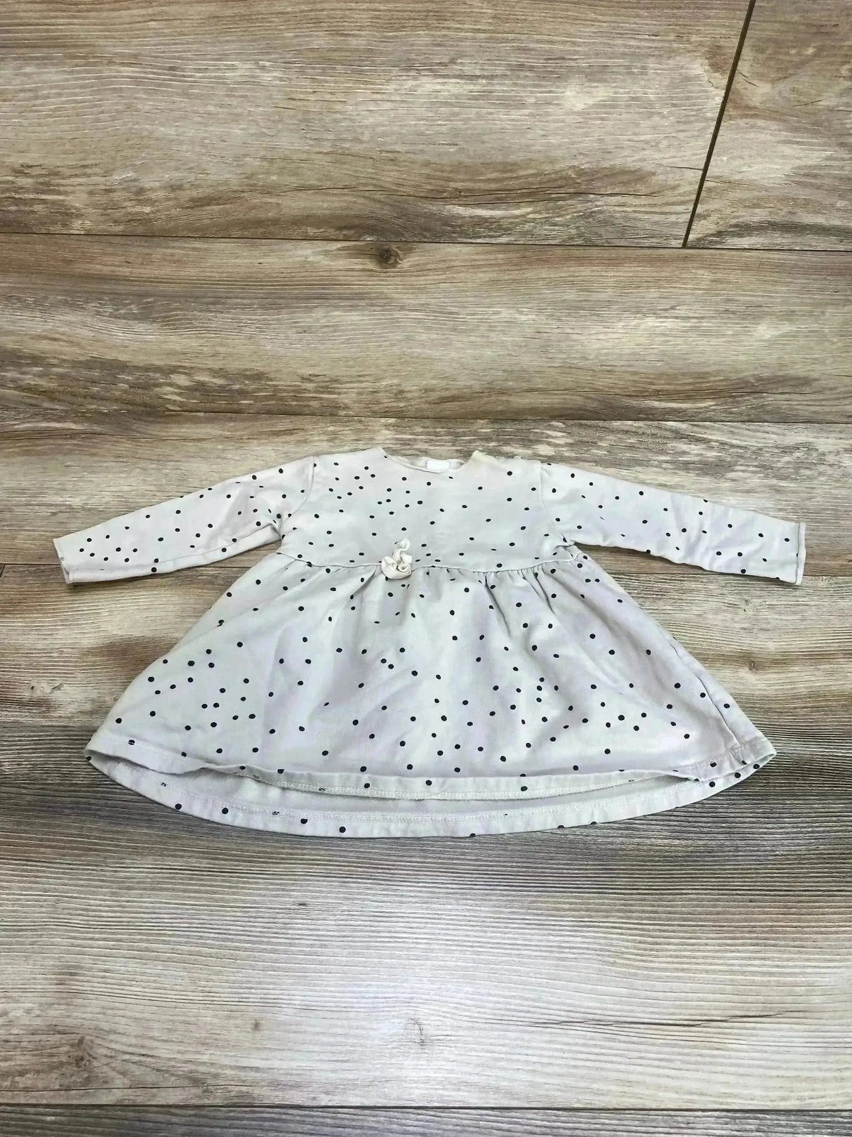 Flat lay of beige long-sleeve baby dress with black polka dots and gathered waist flower, size 6-12 months on wood floor