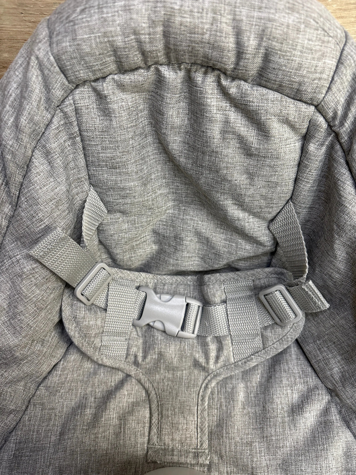 Gray padded baby gear seat with adjustable safety harness and buckle close-up