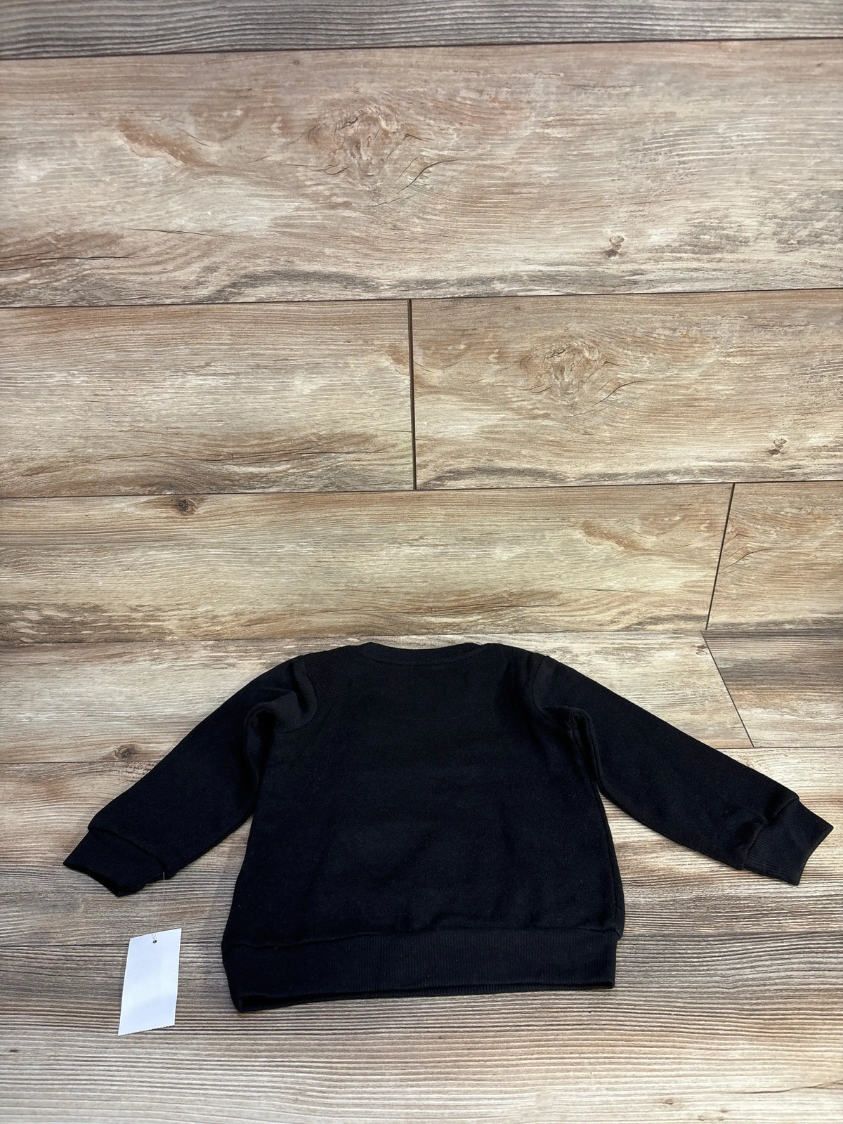 Flat lay of NEW The Notorious B.I.G. sweatshirt in black, size 2T, with long sleeves and ribbed cuffs on wood-look flooring
