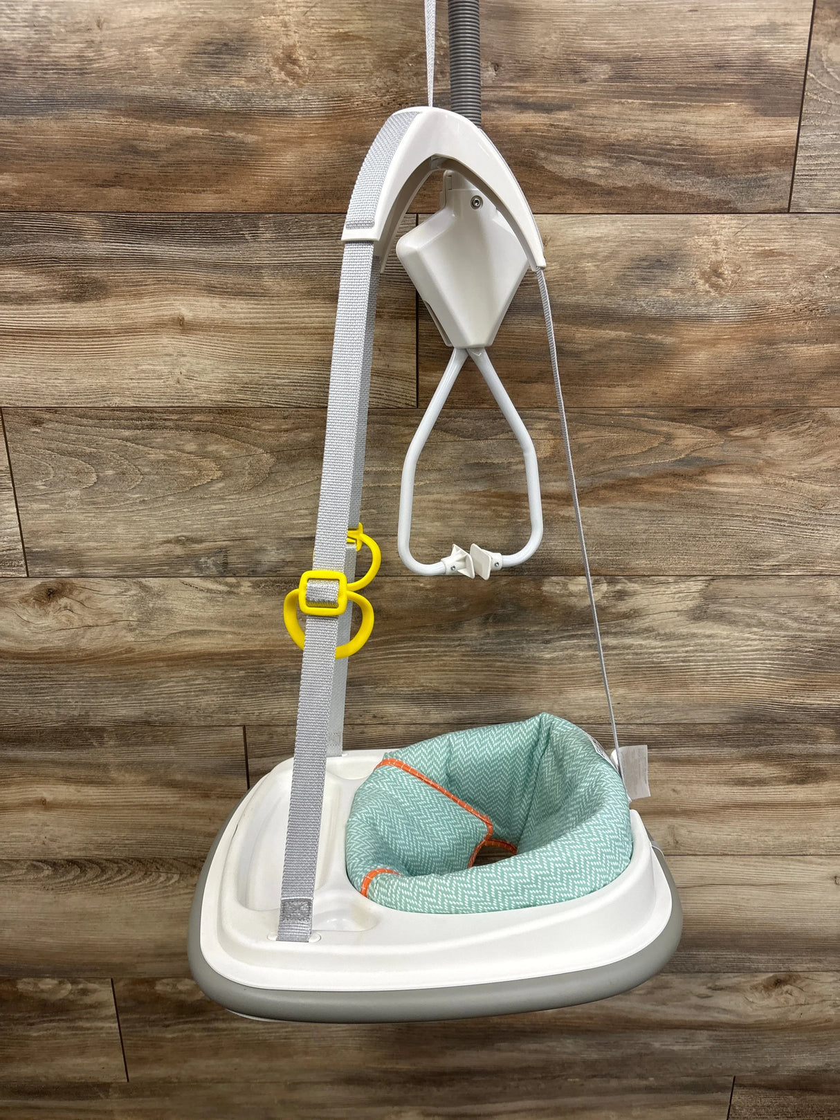 Front view of Graco Caravan doorway bumper jumper showcasing mint green textured seat white frame and yellow buckle clamp against wood plank wall