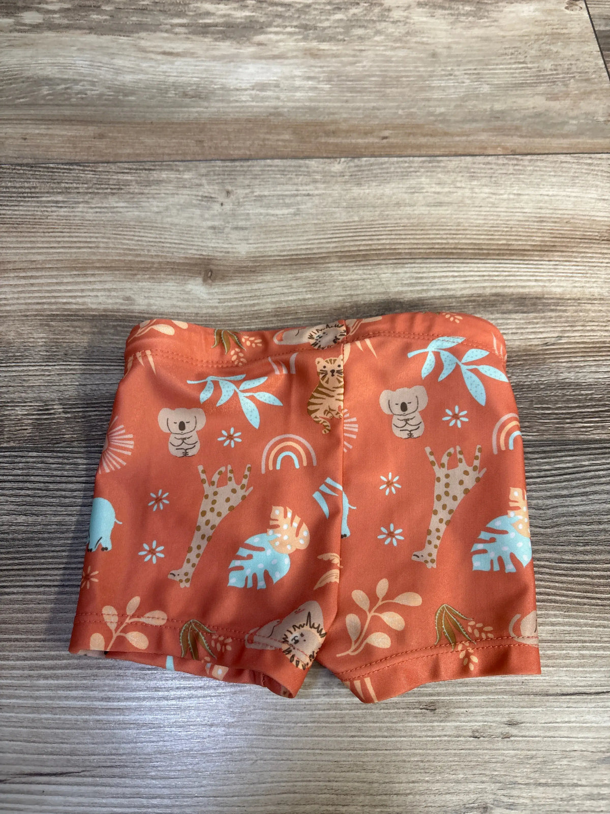Front view of H&M orange animal print swim shorts for ages 9 to 12 months showing elastic waistband on a wood background