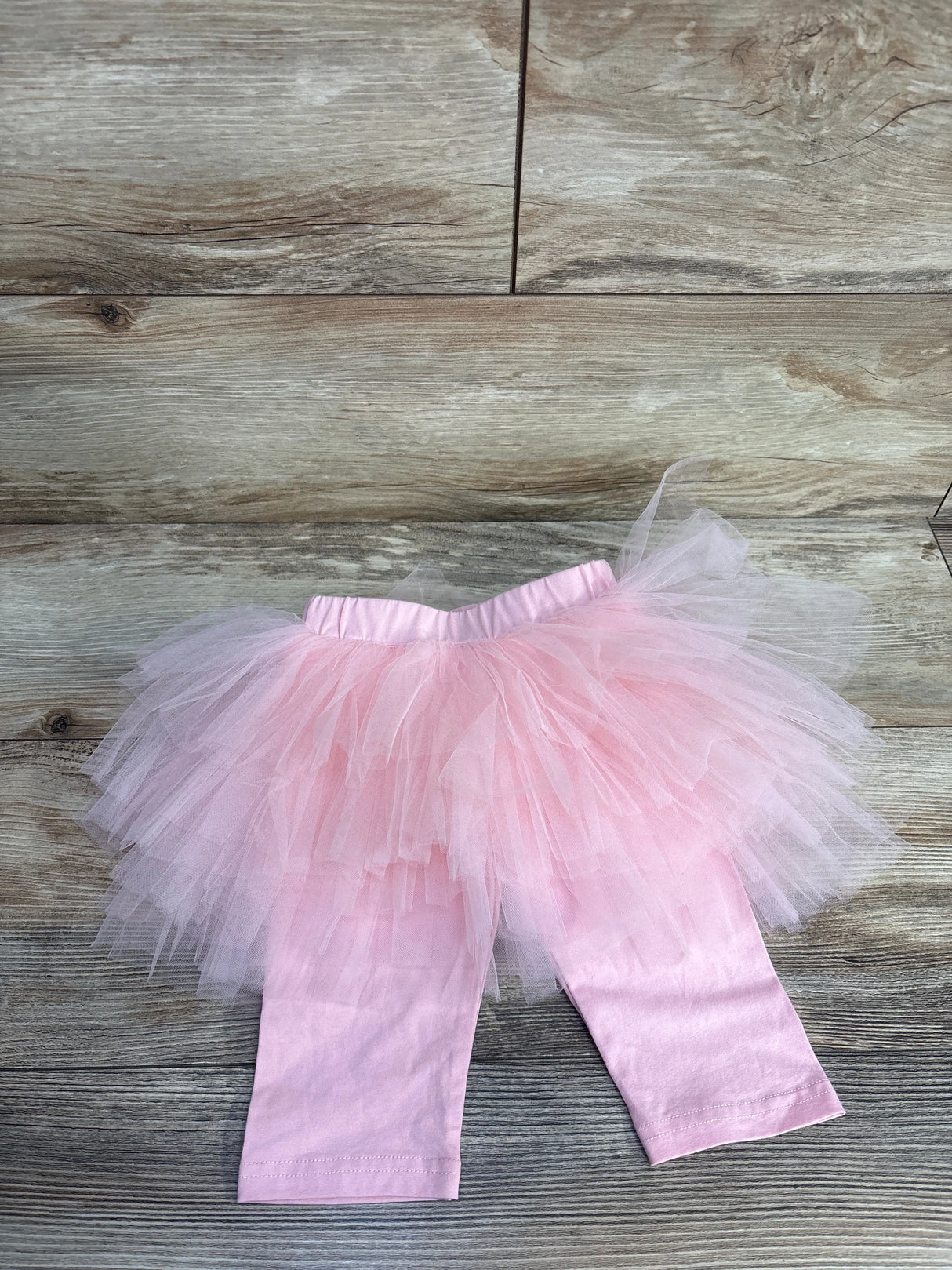 Pink baby tutu leggings with tulle skirt on wooden floor background