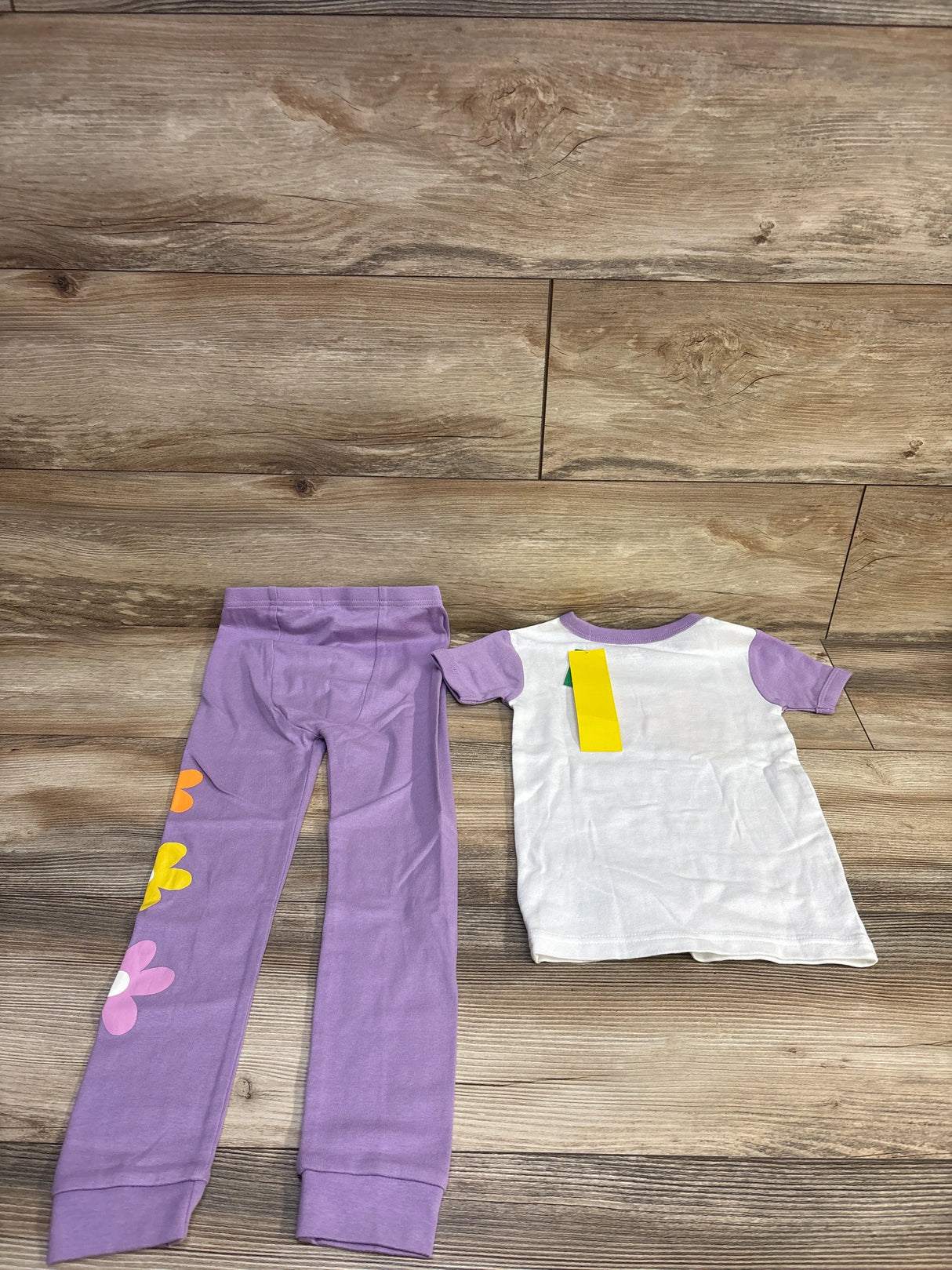 Flat lay of Baby Gap 2pc pajama set: white top with purple sleeves and purple leggings with colorful flower prints on wood floor