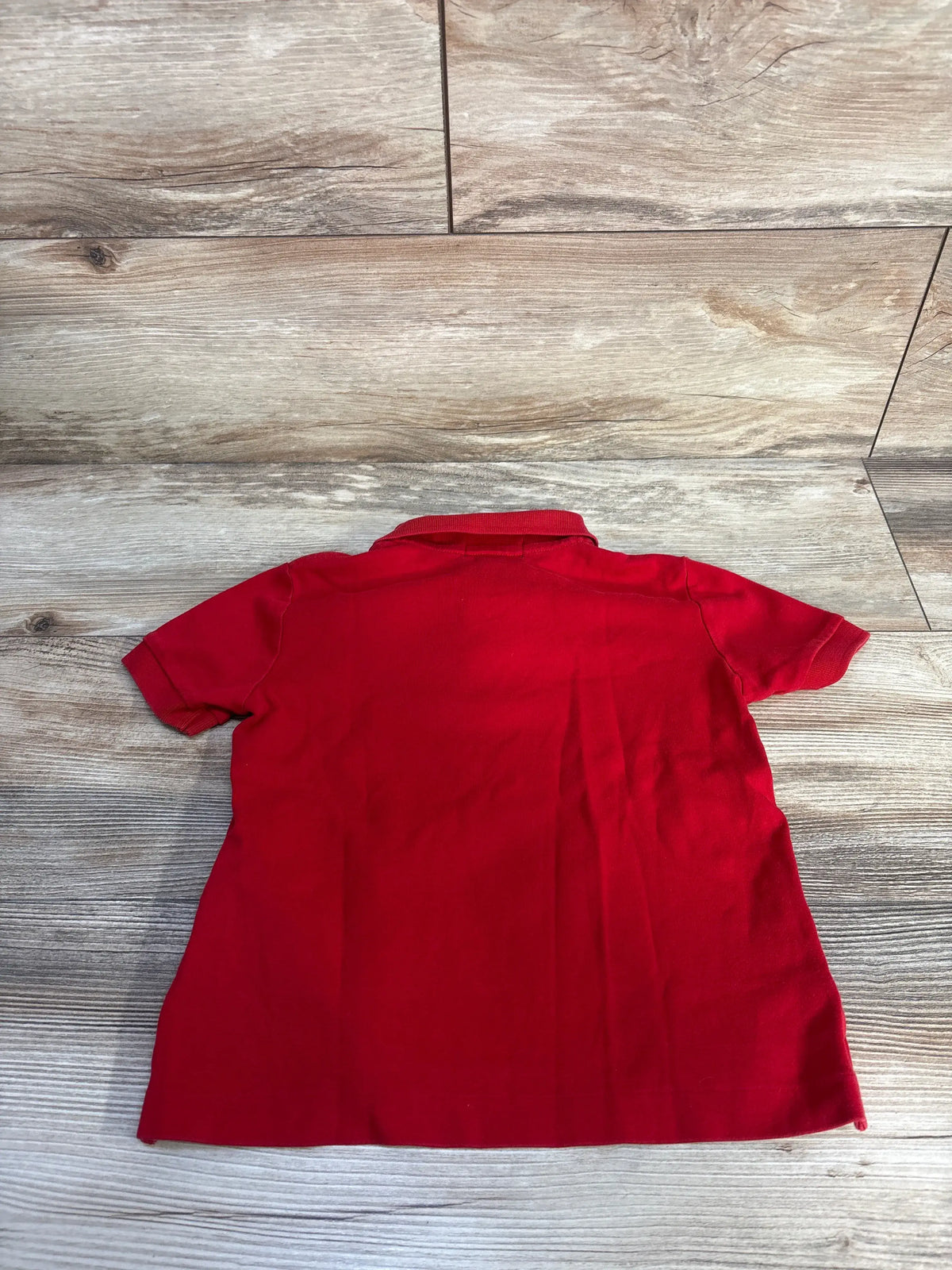 Back view of Polo Ralph Lauren red polo shirt in size 3T showcasing short sleeves and collar with wood-look flooring background