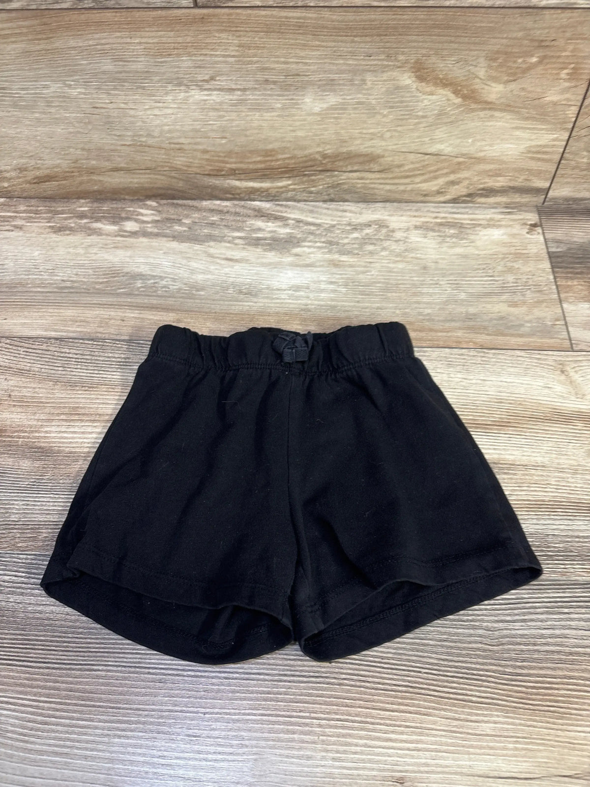 Front view of Children’s Place black drawstring shorts size 5-6T showcasing adjustable drawstring waist on a wood floor