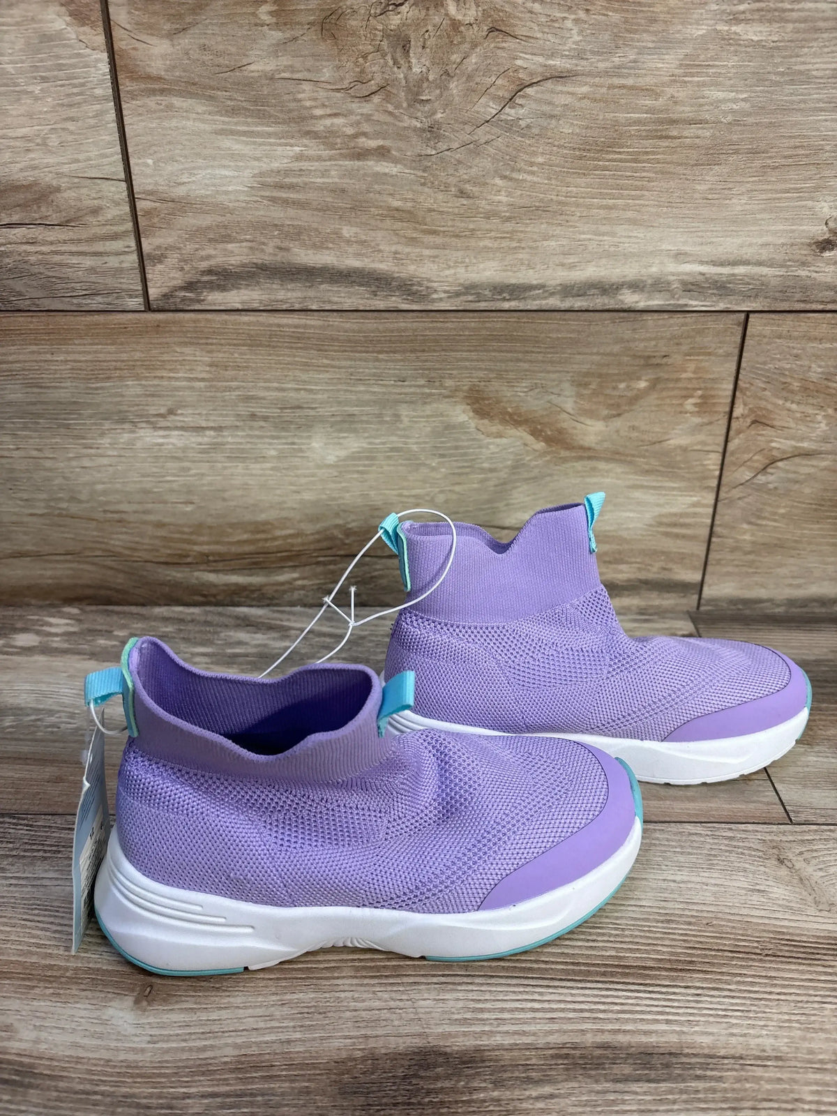 Side view of Cat & Jack Ari purple slip-on knit kids sneakers with sock-like ankle, white sole, and teal pull tabs on wood background