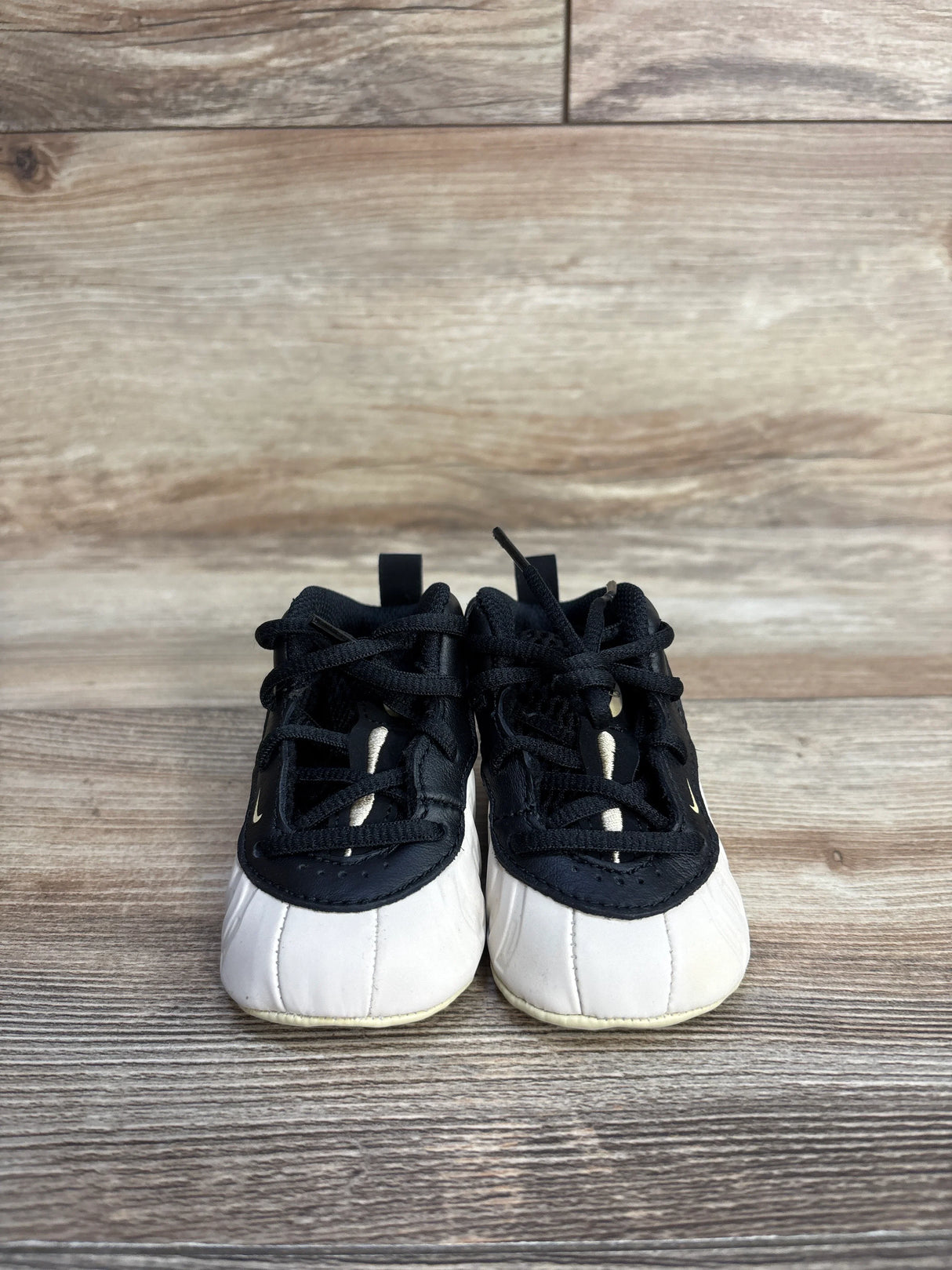Black and white baby sneakers with laces on wood floor background
