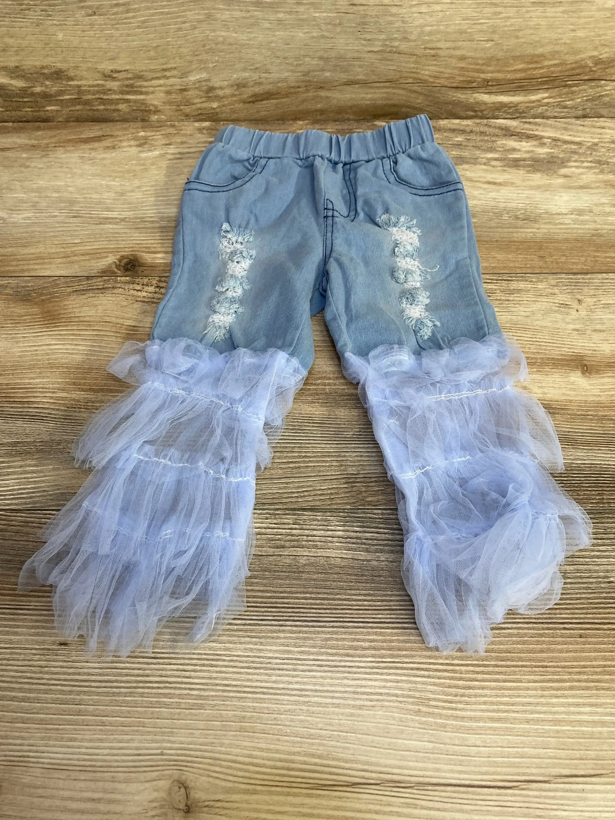 Flat lay of baby 12-month light blue distressed jeans with elastic waist and white tulle ruffle bell bottoms on wood background