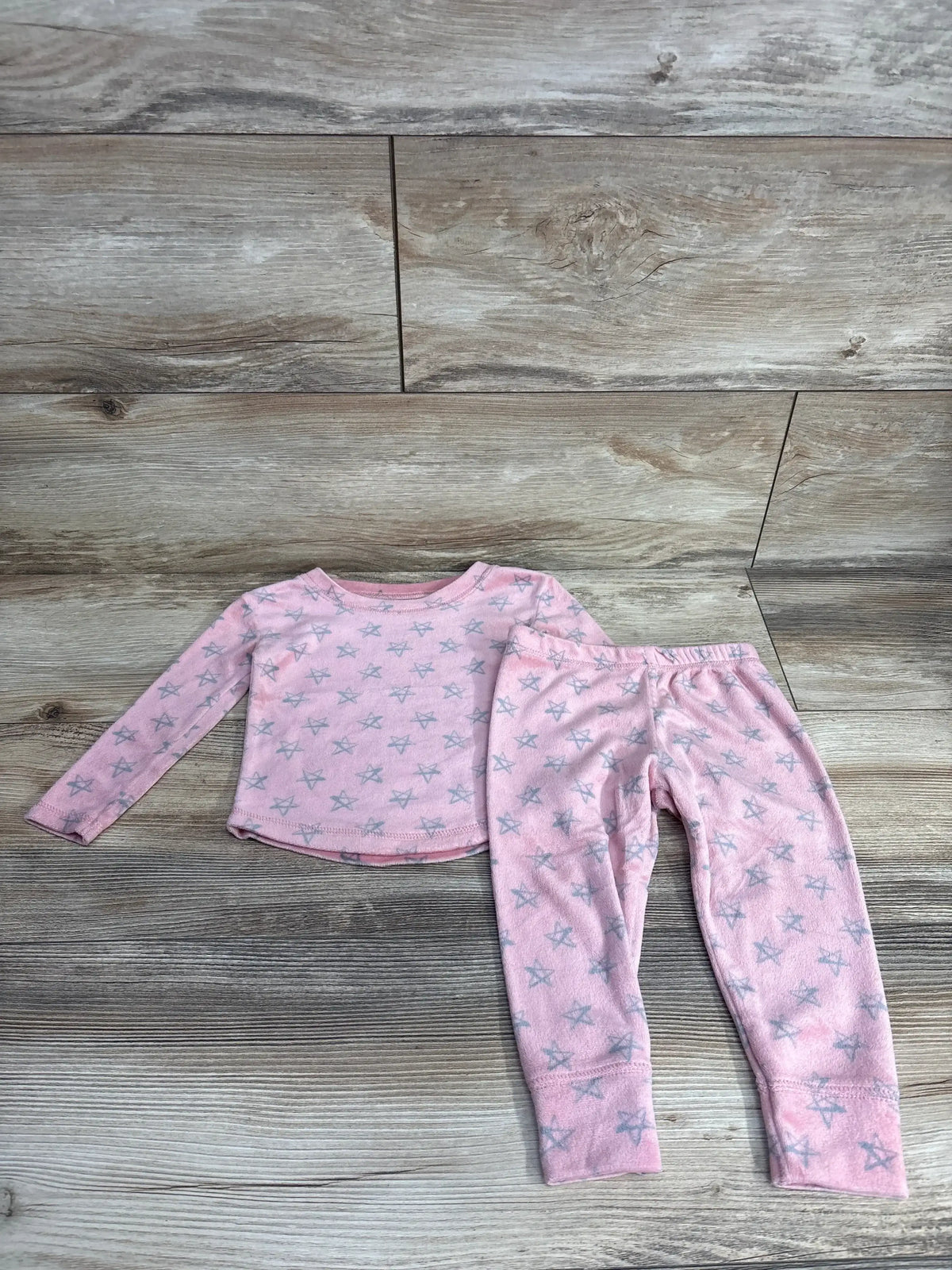 Pink children's long-sleeve pajama set with gray star pattern on wooden floor