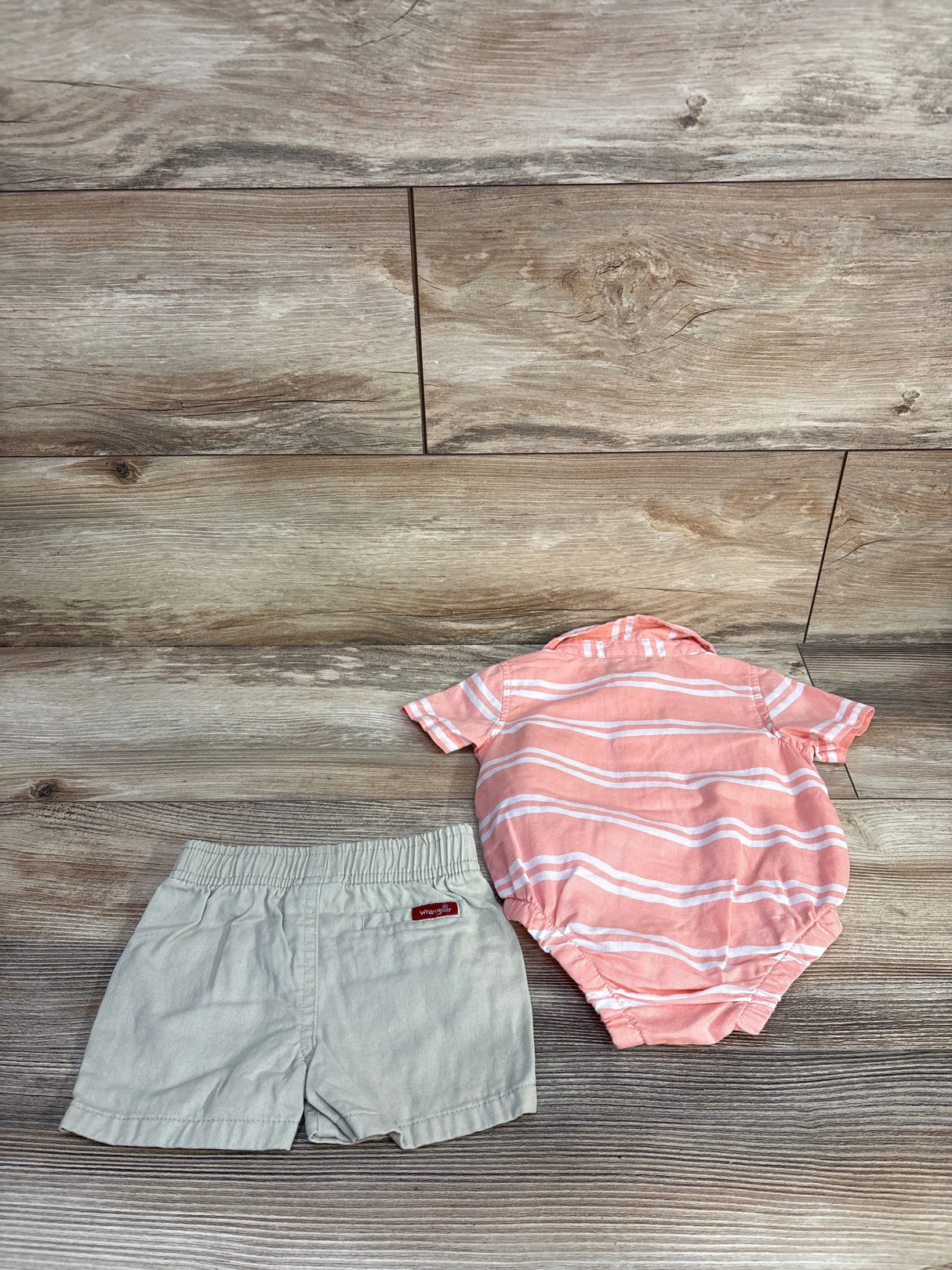 Flat lay of pink and white striped baby polo bodysuit with snap crotch and beige shorts with elastic waist on light wood background