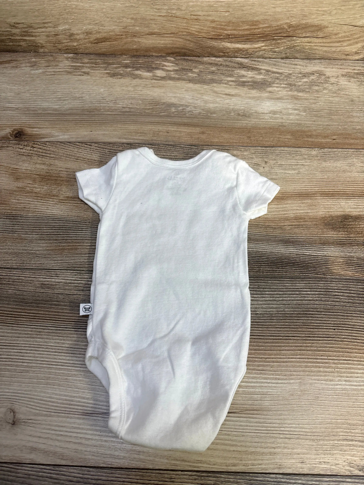 Top view of Honest Baby white bodysuit in 0-3 months showcasing short sleeves and rounded neckline with a wood-grain background