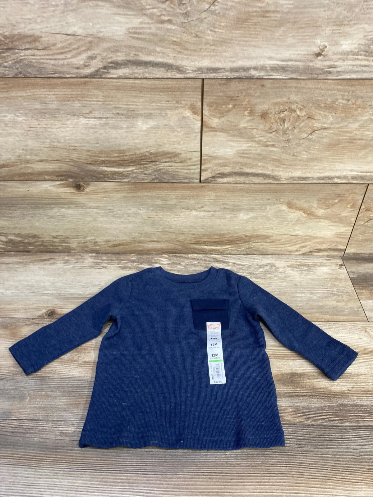 Front view of Jumping Beans long-sleeve navy blue toddler shirt showcasing chest pocket and attached 12M size tag on wood background