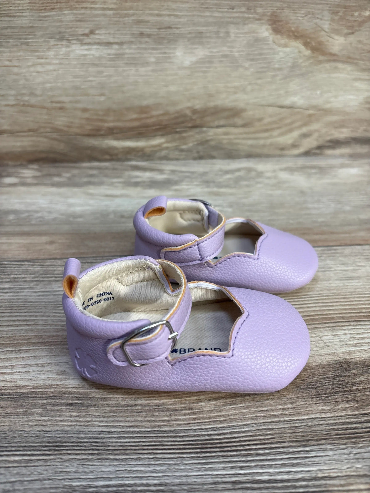 Front and side view of Lucky Brand purple Mary Jane crib shoes with hook and loop closures and pull tabs on wood grain