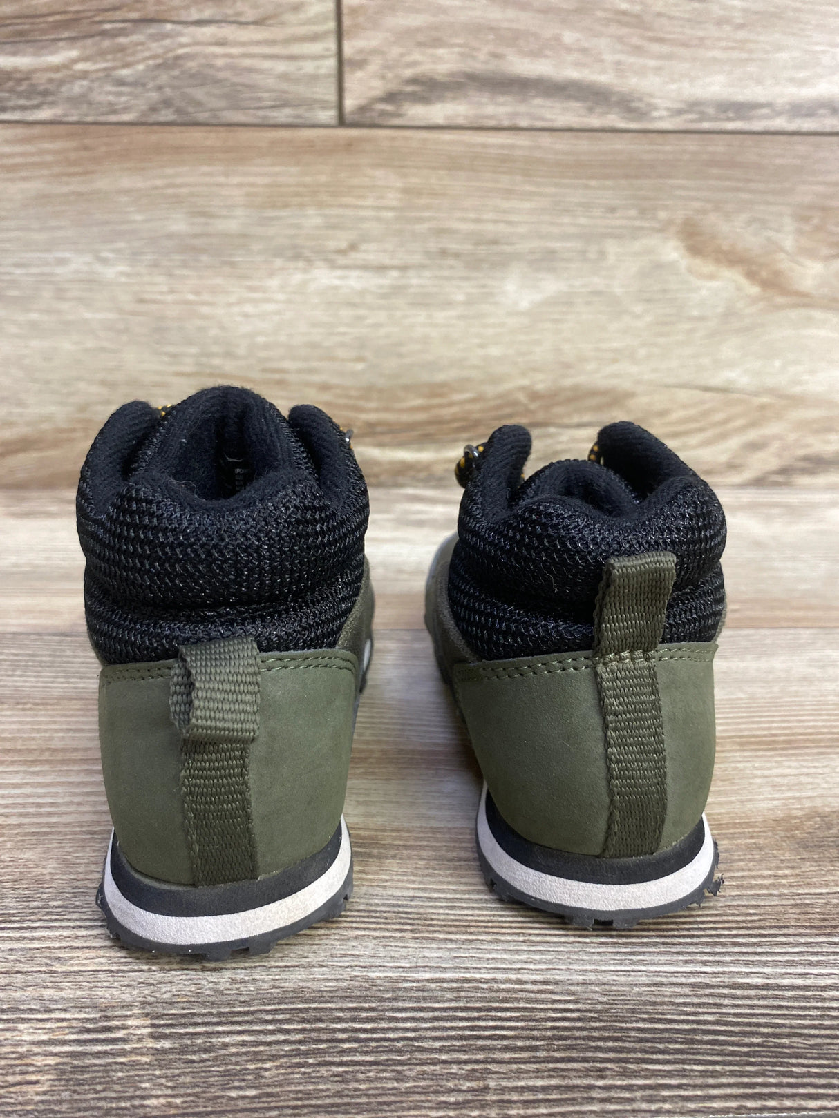Back view of children's olive green and black hiking boots on wooden surface