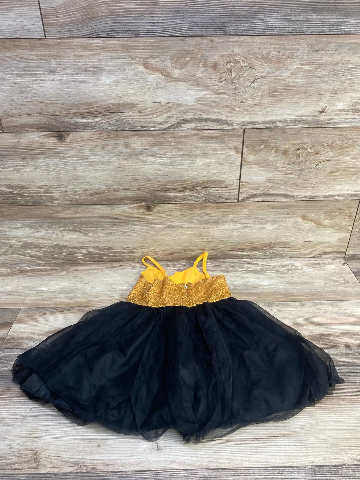 Flat lay of toddler gold sequin bodice dress with yellow lining and thin straps, full black tulle skirt on light wood floor