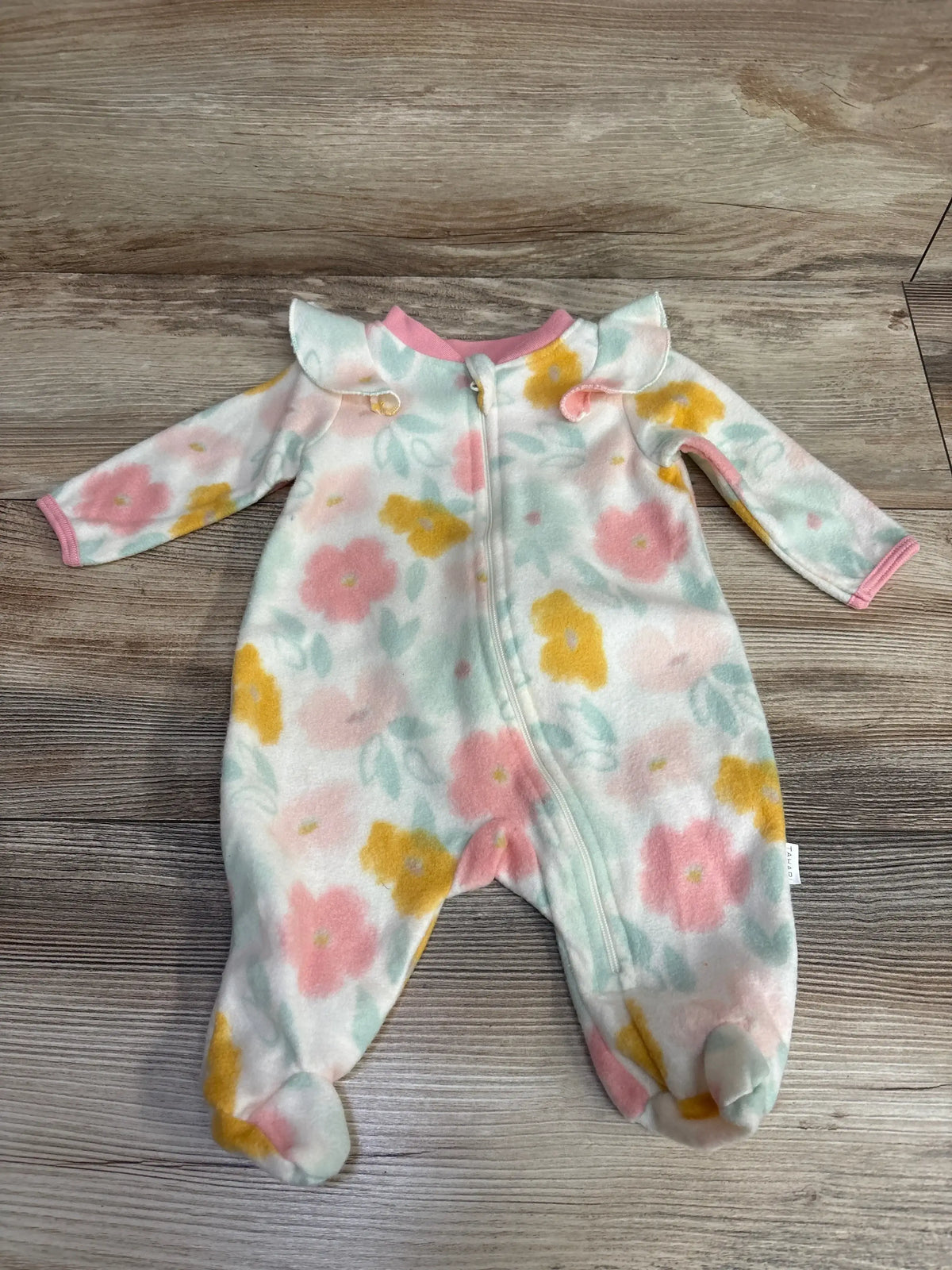 Floral baby fleece footed sleeper with pastel pink, yellow, and green flowers and pink trim on wooden floor