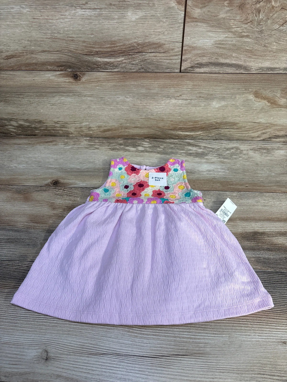 Front view of pink baby dress from a dress and bloomers set showcasing floral crochet panel and crinkled jacquard skirt