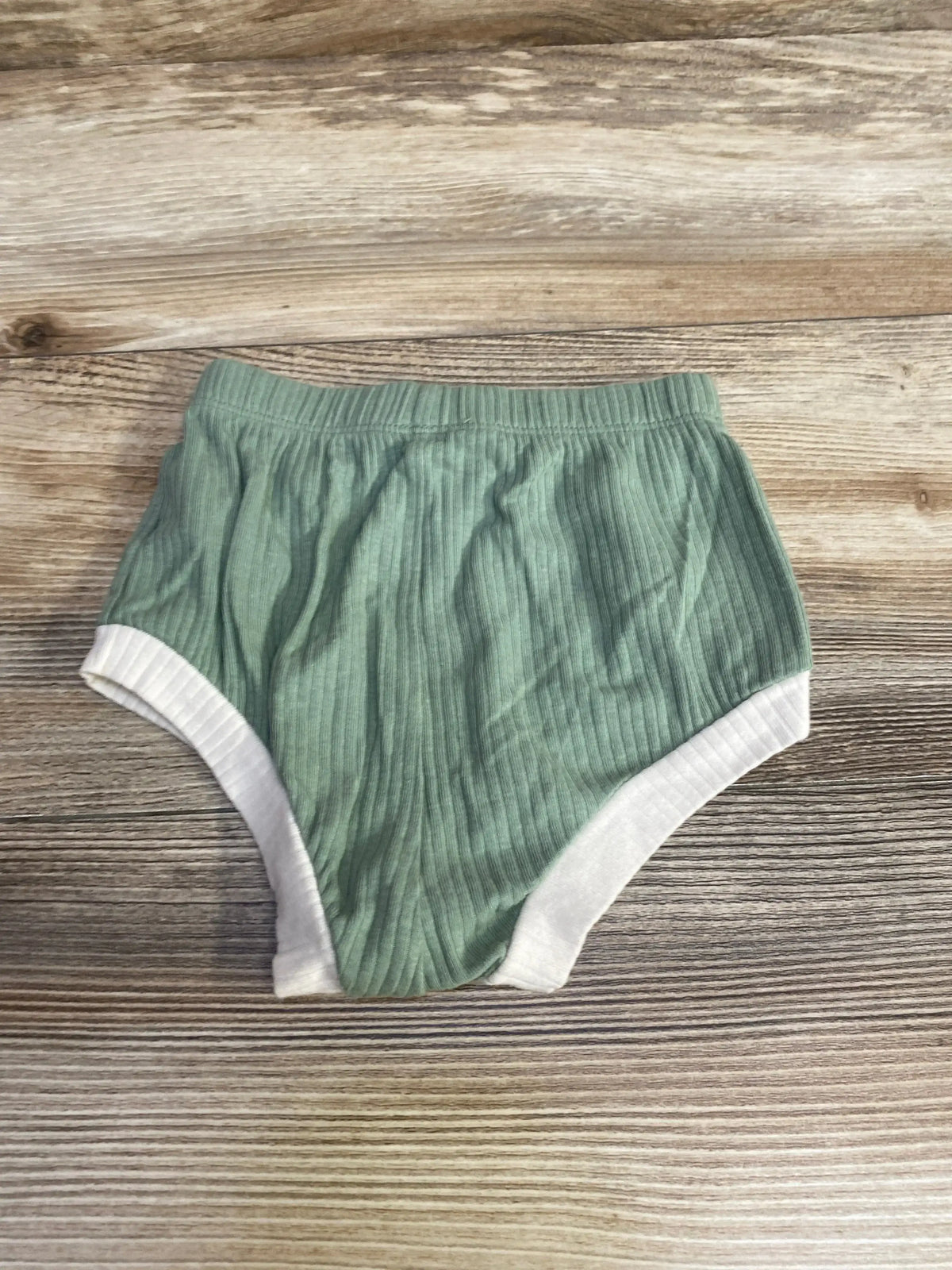 Top down view of green Cat and Jack baby bloomers showcasing ribbed fabric and white leg trim on a wood background