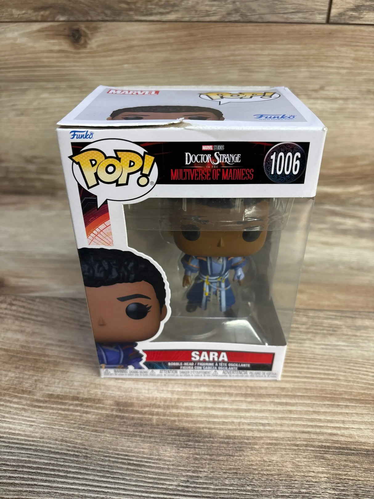 Three-quarter front view of boxed Funko Pop Sara showcasing the bobble-head in a blue robe visible through the box’s clear window on a wood surface