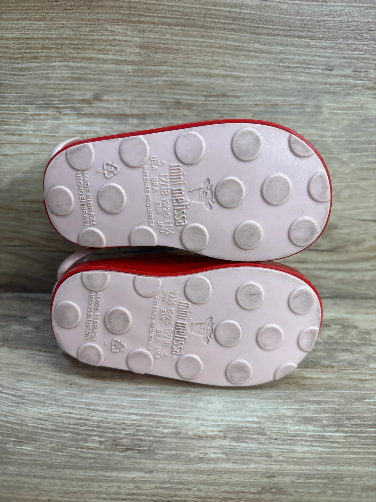 Bottom view of pink Mini Melissa toddler shoes with polka dot textured soles on wood