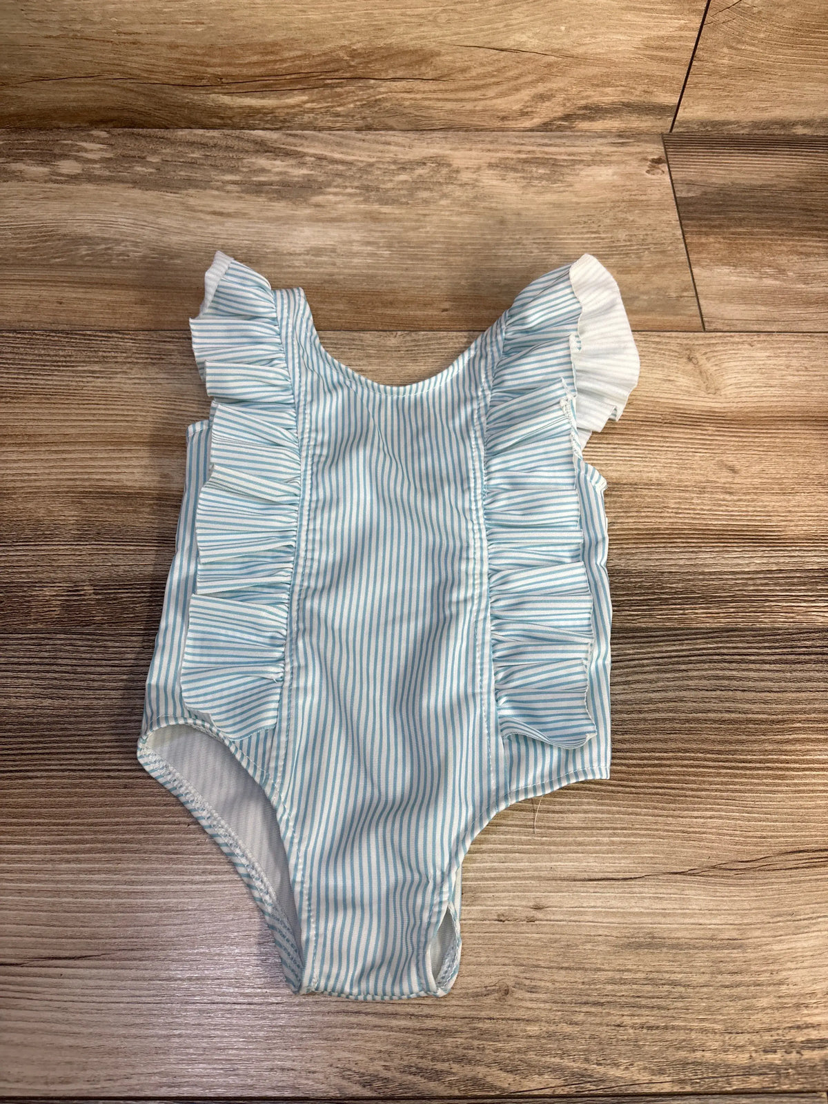 Front view of the white striped ruffle one piece swimsuit, size 2T, showcasing light blue stripes and shoulder ruffles on a wood background