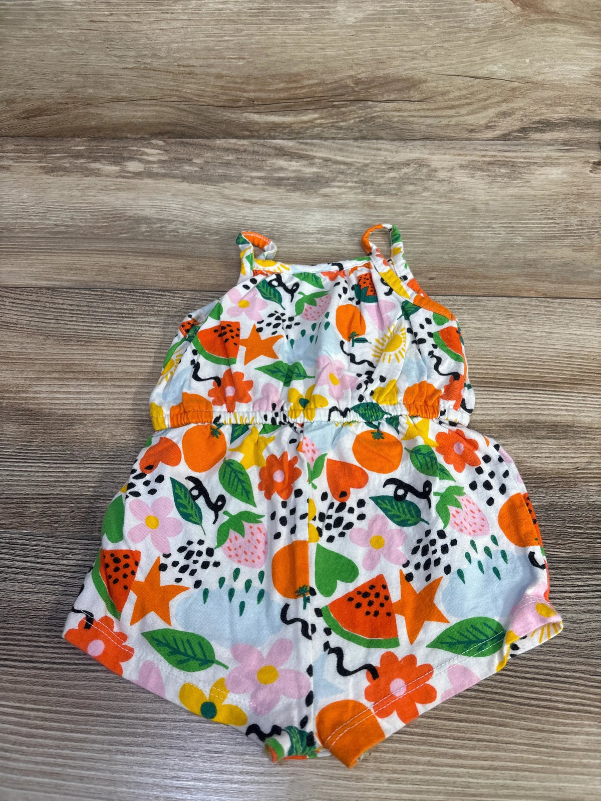 Front view of Baby Gap Mixed Fruit Print Sleeveless Jersey-Knit Romper in white showcasing colorful fruit and floral print with spaghetti straps on wood plank floor