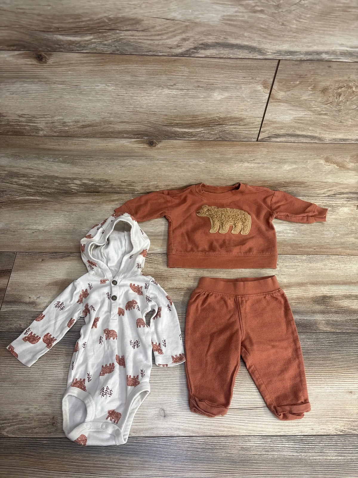 Baby bear print hooded onesie, matching rust pants and sweatshirt set on wooden floor