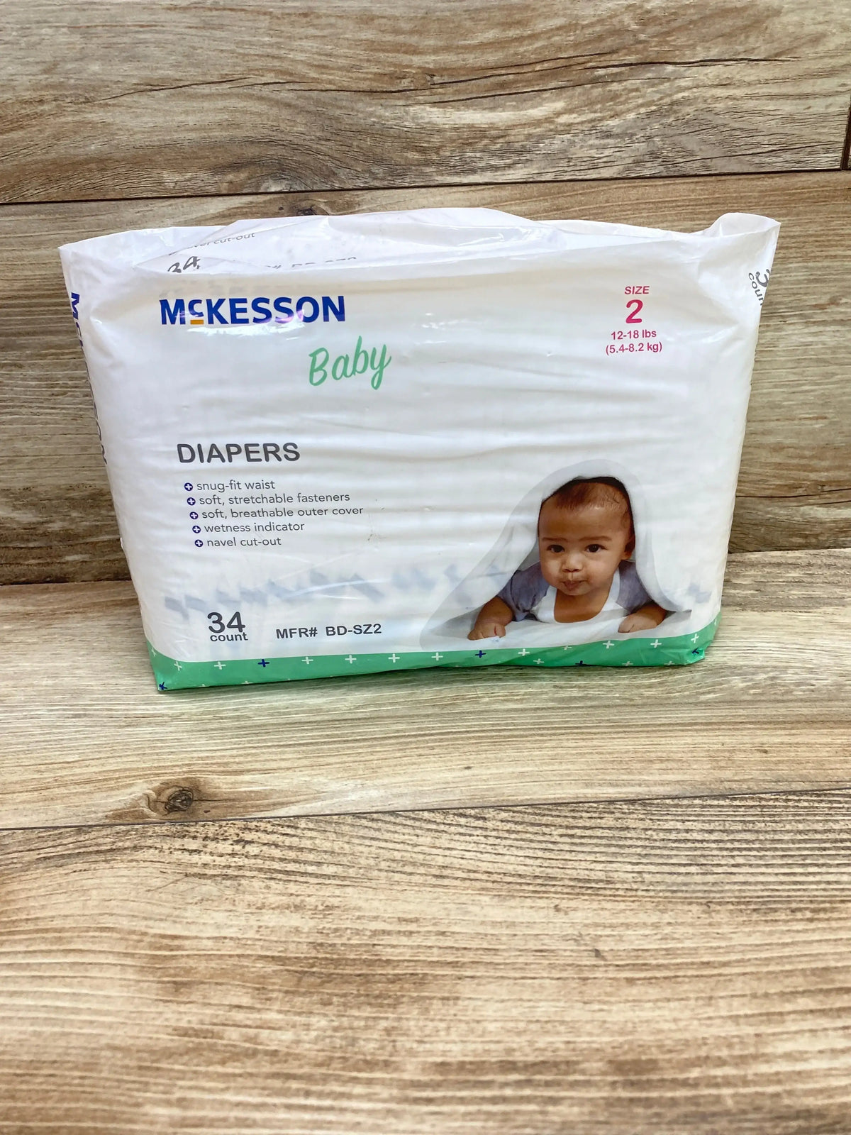 Front of McKesson Baby Diapers Size 2 showing baby photo and label: snug-fit waist and wetness indicator on wood background