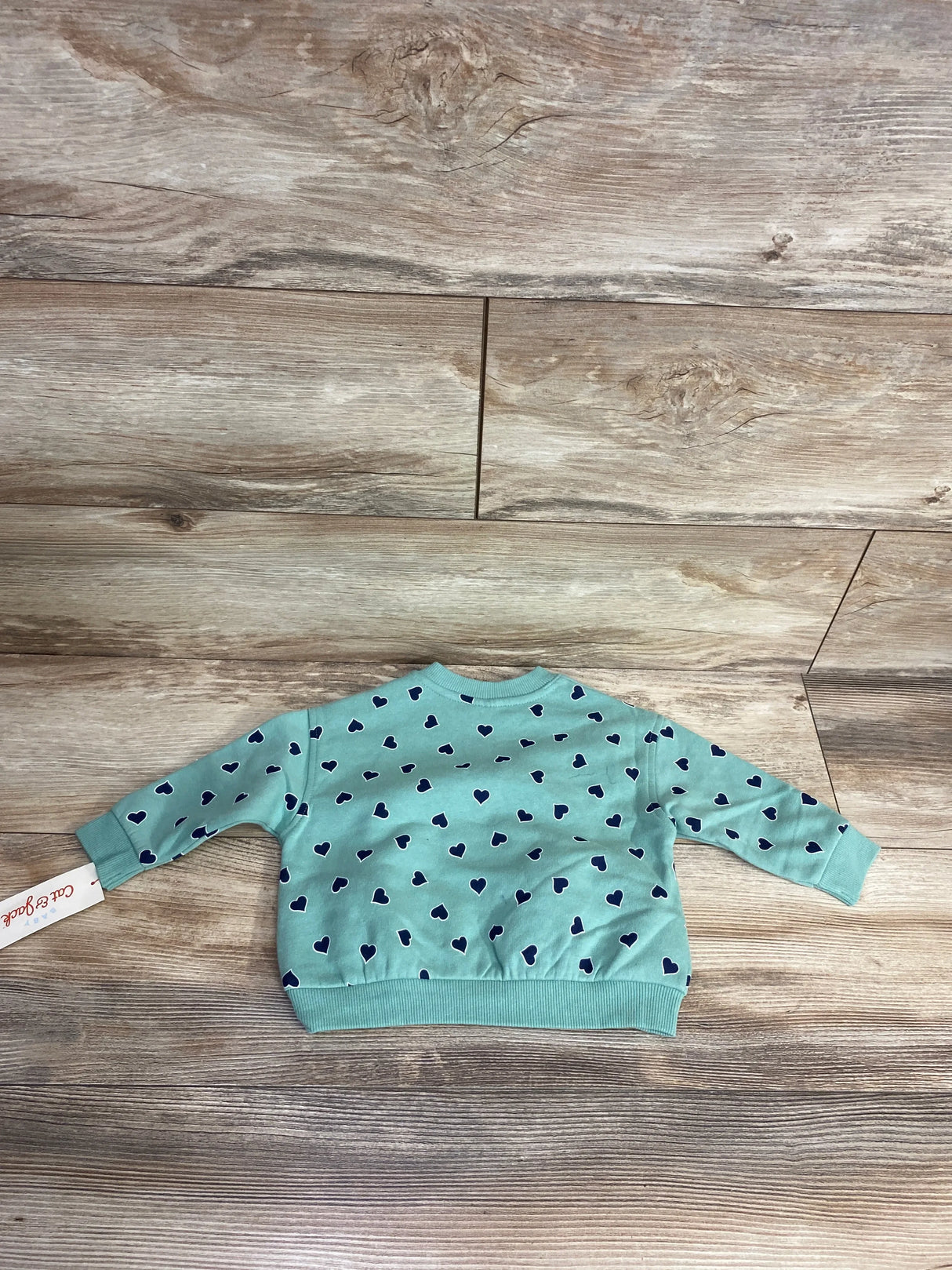 Baby blue sweatshirt with navy heart pattern laid flat on wooden floor, kids clothing