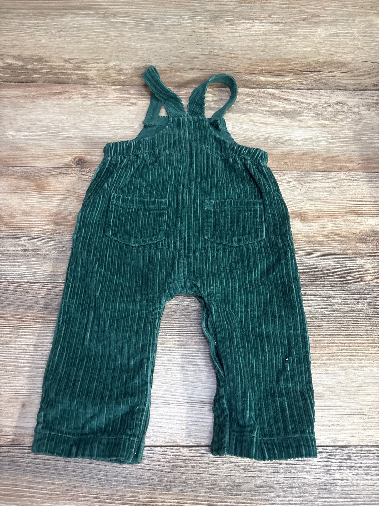 Green corduroy overalls for toddlers with front pockets on wooden background