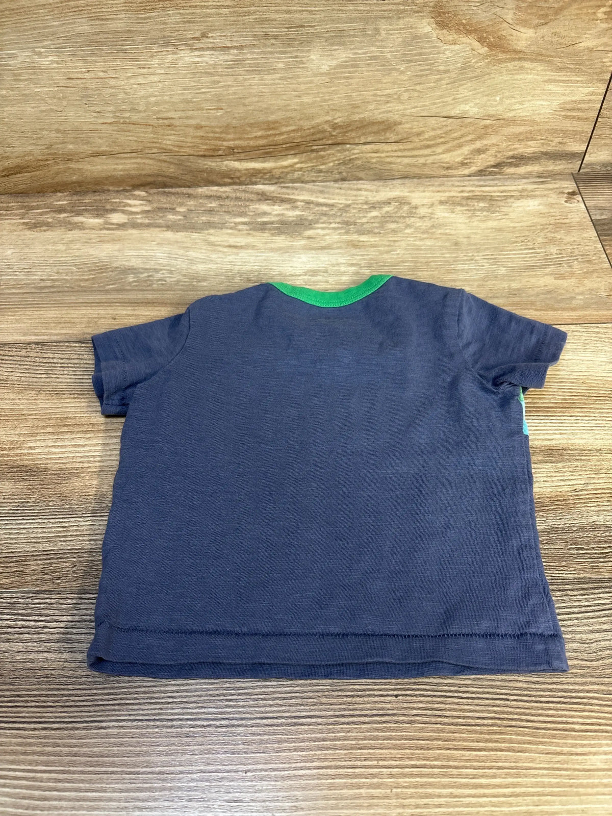 Navy blue short sleeve toddler t-shirt with green neckline on wood background
