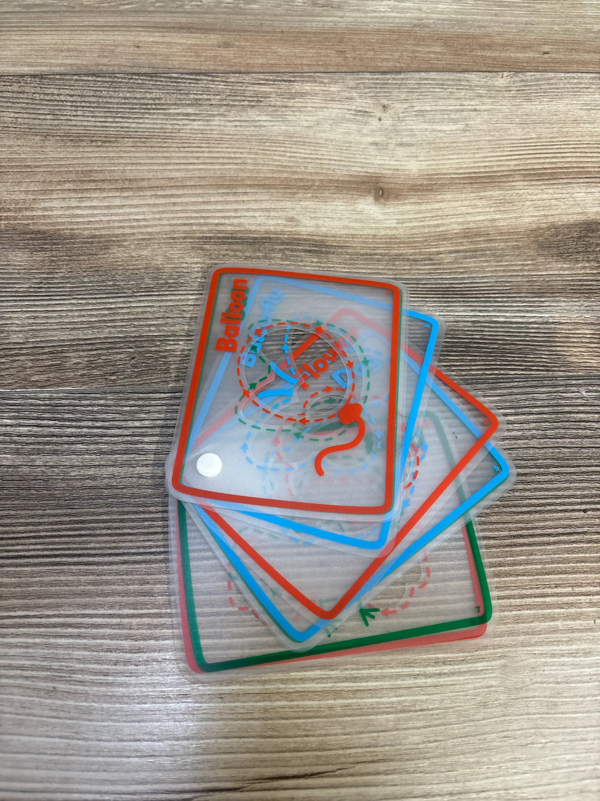 Angled view of 8 translucent tracing cards stacked, colored borders and dashed tracing paths, Balloon on wood table