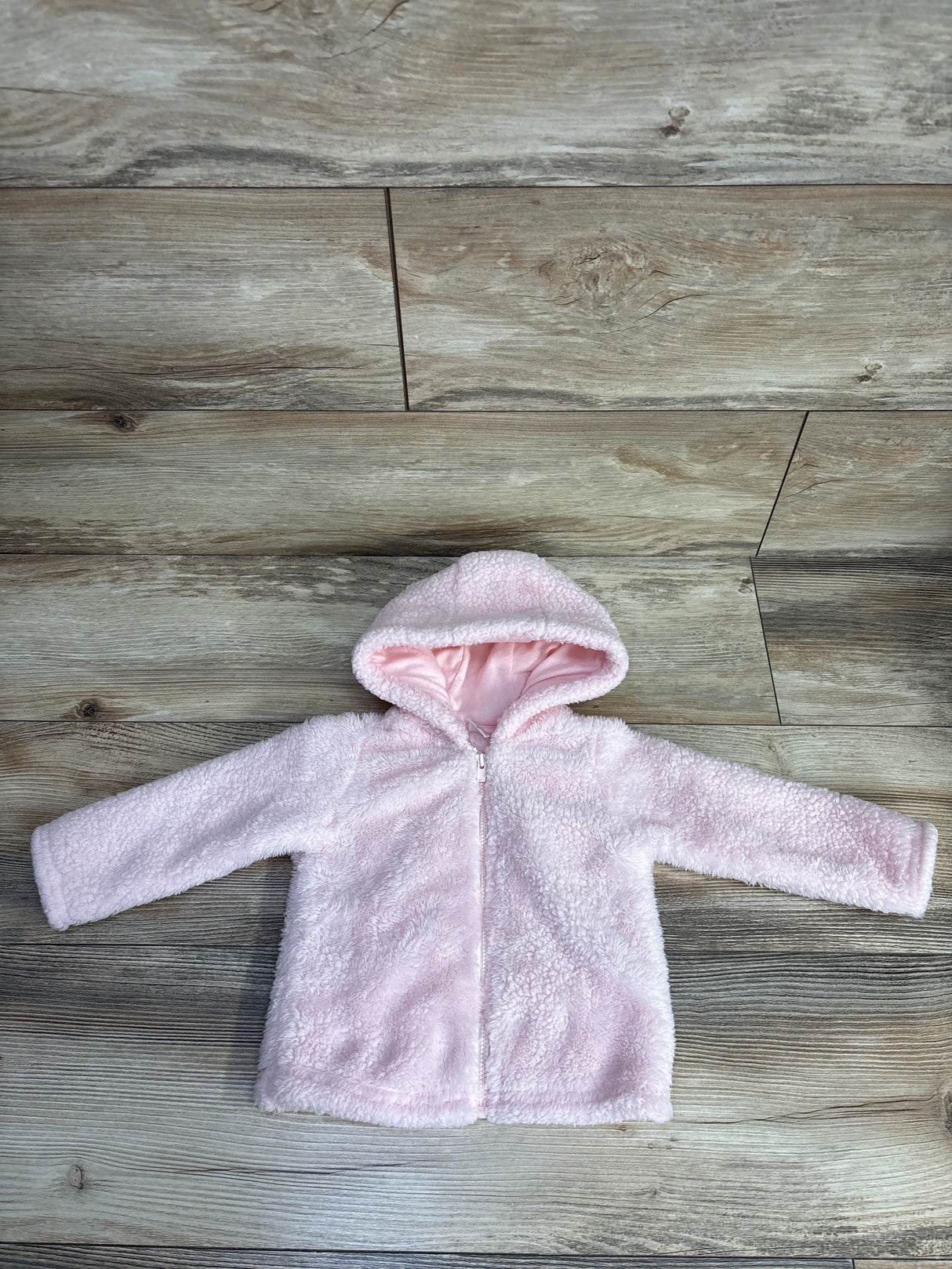 Soft pink toddler hooded fleece jacket laid flat on wooden floor background