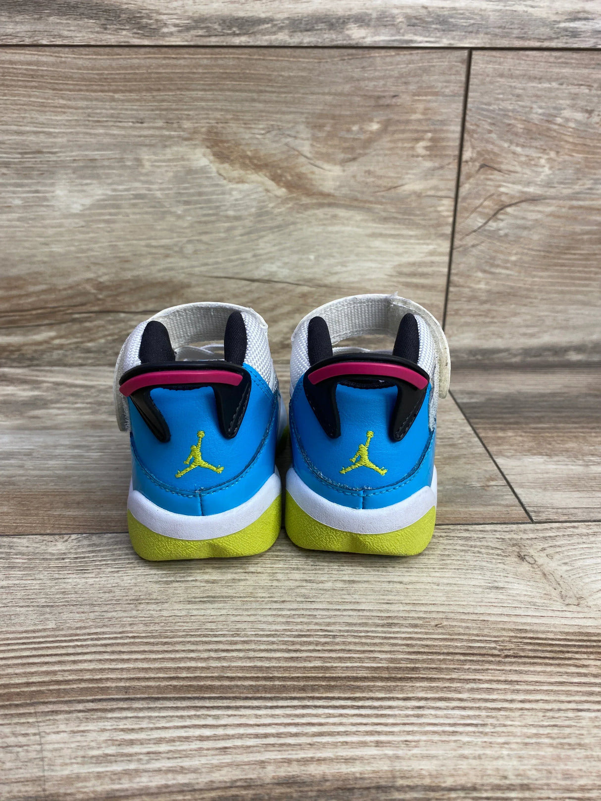 Rear view of Air Jordan 6 Rings TD toddler sneakers showing blue upper, yellow sole, neon Jumpman and white Velcro strap on wood floor