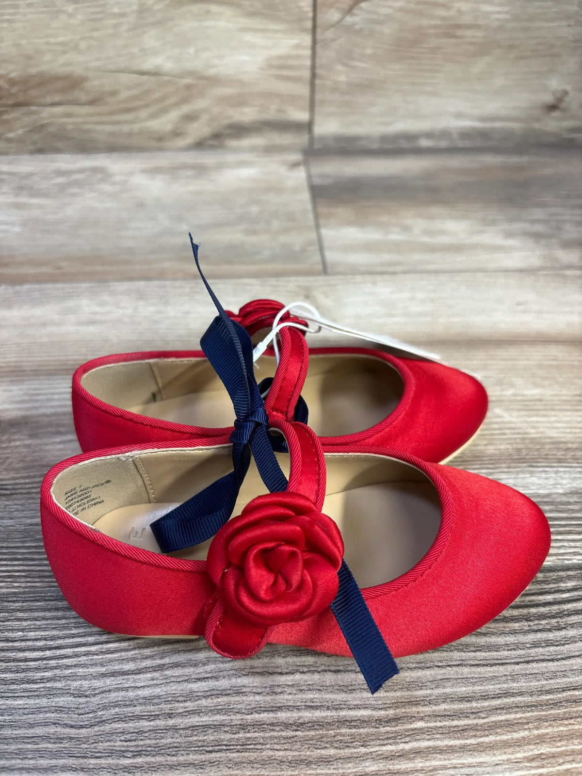 Top view of Janie & Jack satin red ballet flats showcasing a satin rosette and navy ribbon tie on wood background