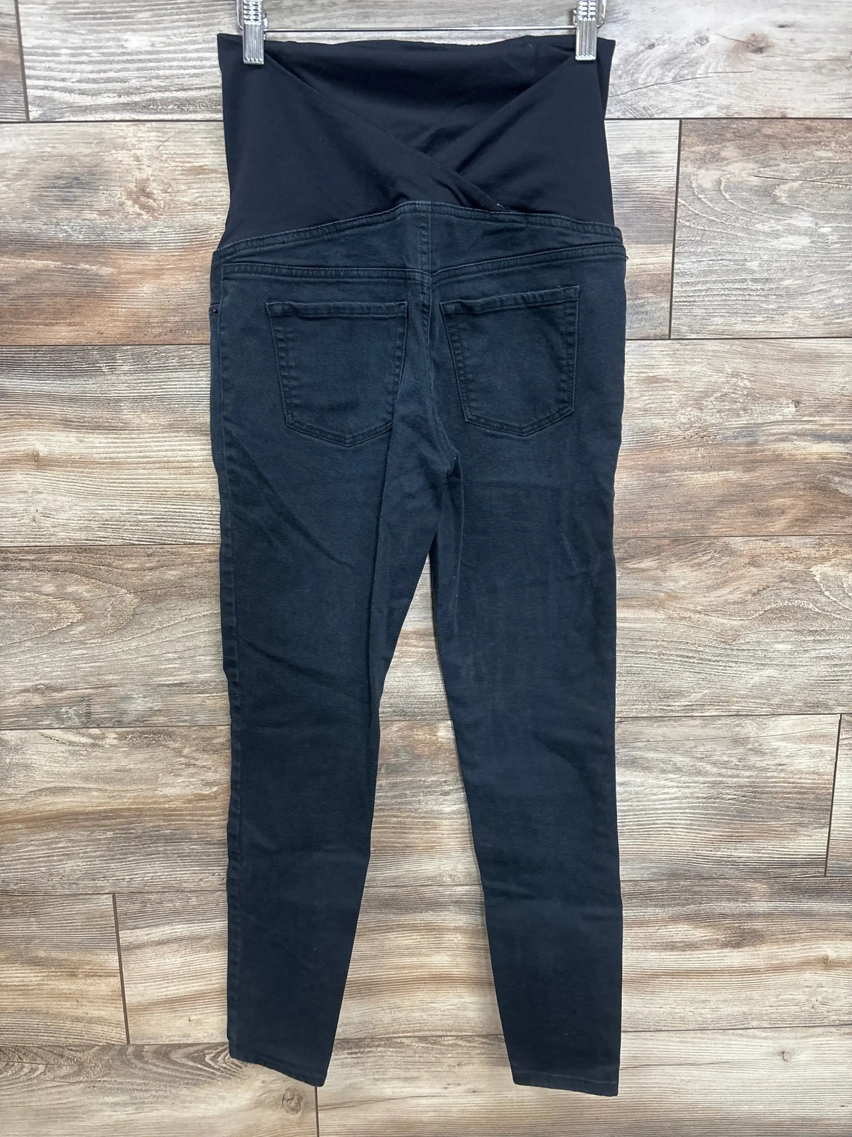 Back view of Isabel maternity crossover-panel skinny jeans in black showcasing the crossover belly panel and back pockets with a wood floor background