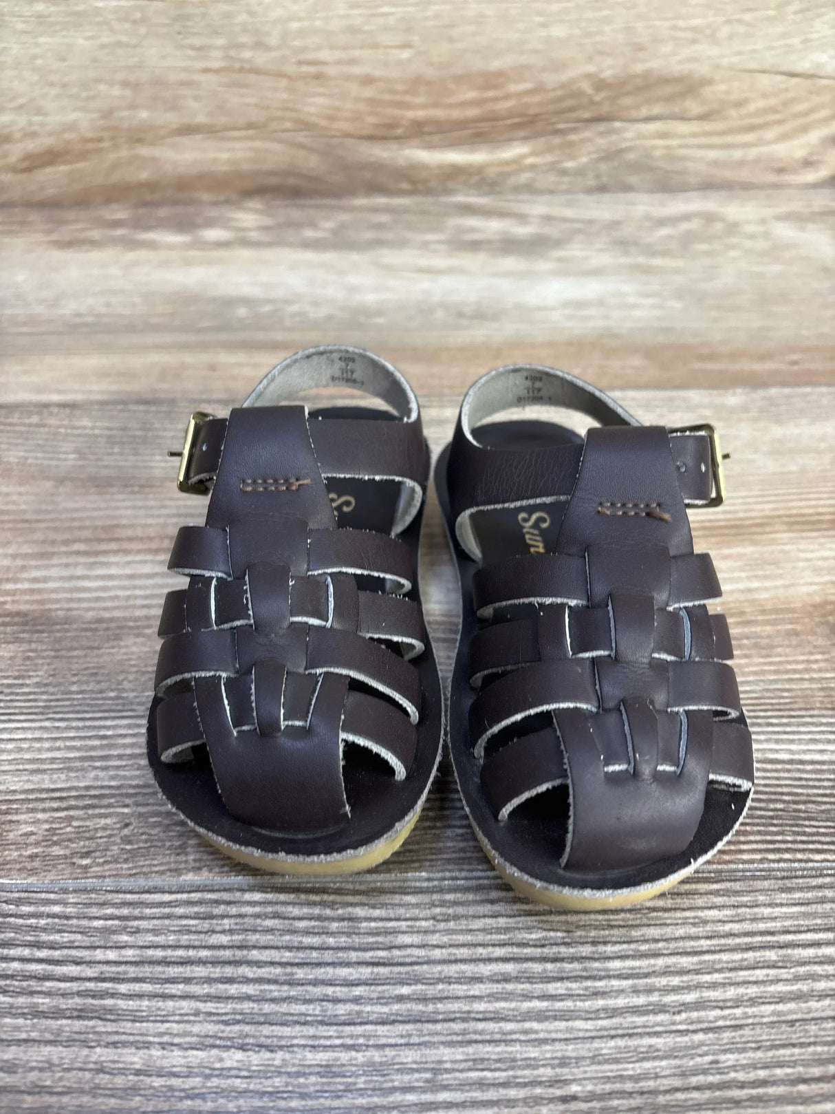 Front view of brown Sun-San sailor sandals size 7C showing woven leather straps and buckle on wood floor
