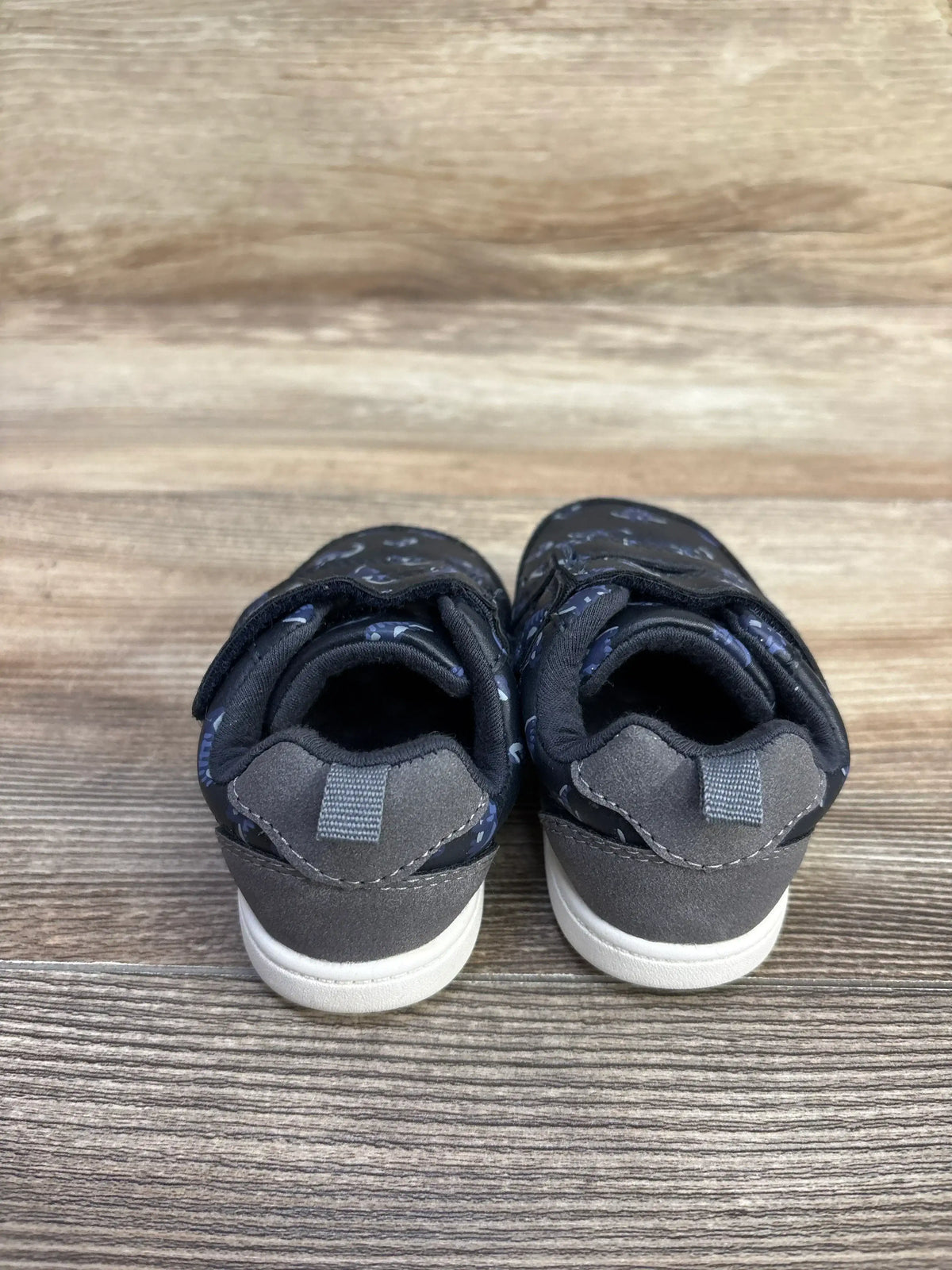 Rear view of Carter’s Every Step First Walker Neo Dino sneakers in navy showcasing pull tabs on wood-grain background