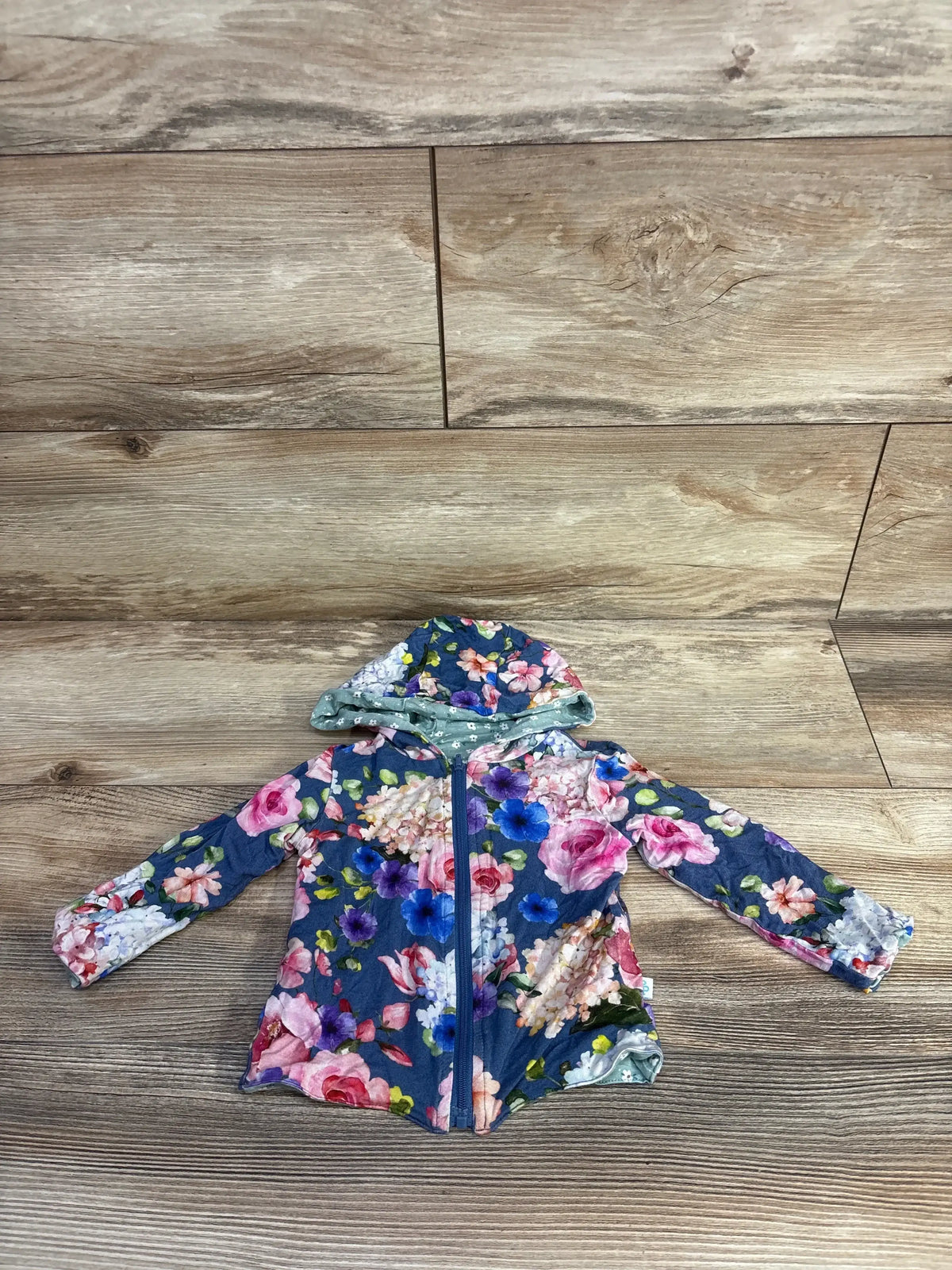 Front view of Posh P reversible hoodie with teal floral print zip up front and pink and blue flowers on wood plank floor
