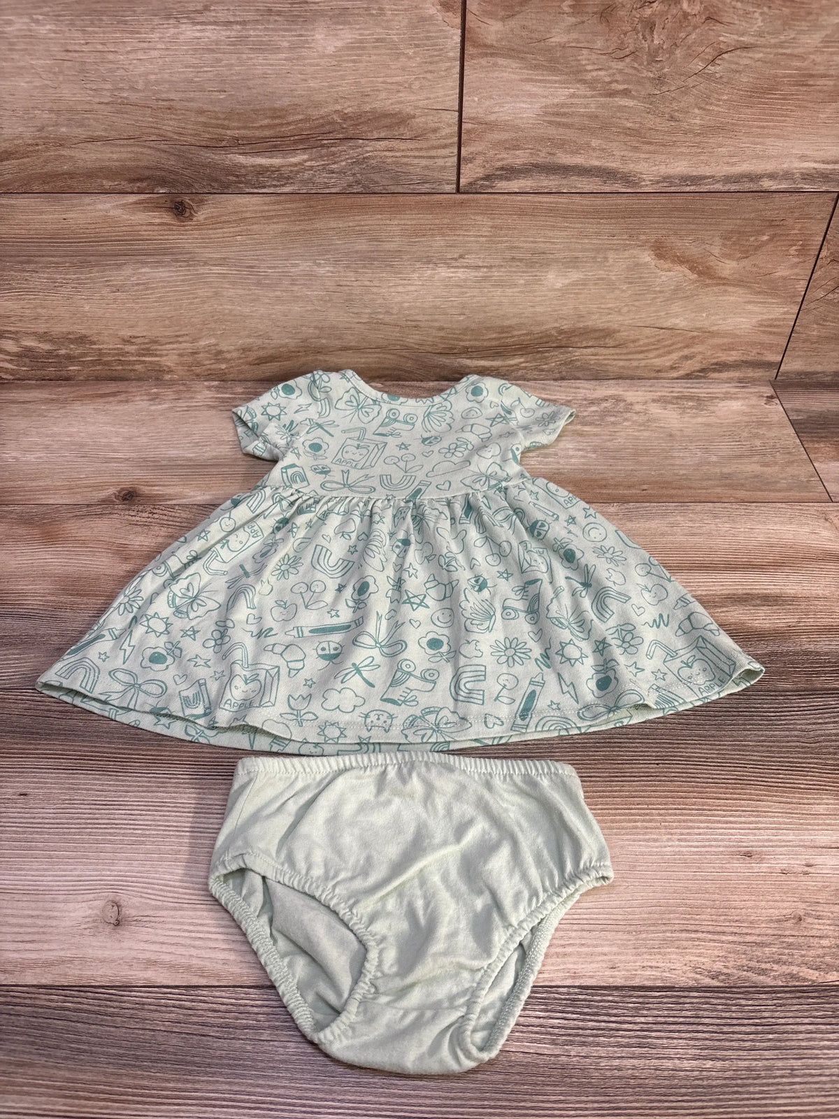 Overhead view of Cat & Jack dress and bloomers set with green patterned dress and matching bloomers on wood-grain background