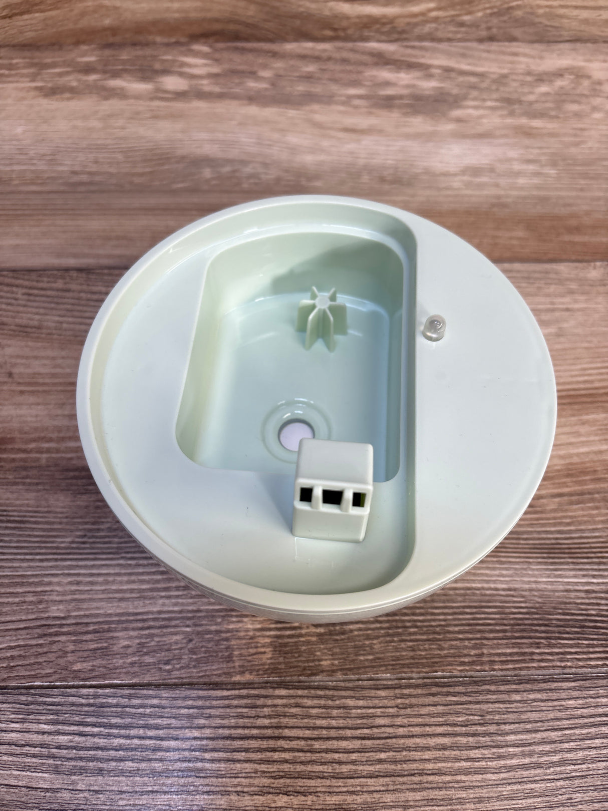 Top view of PureBaby 3-in-1 Humidifier inner lid showing vent and connector on wooden surface