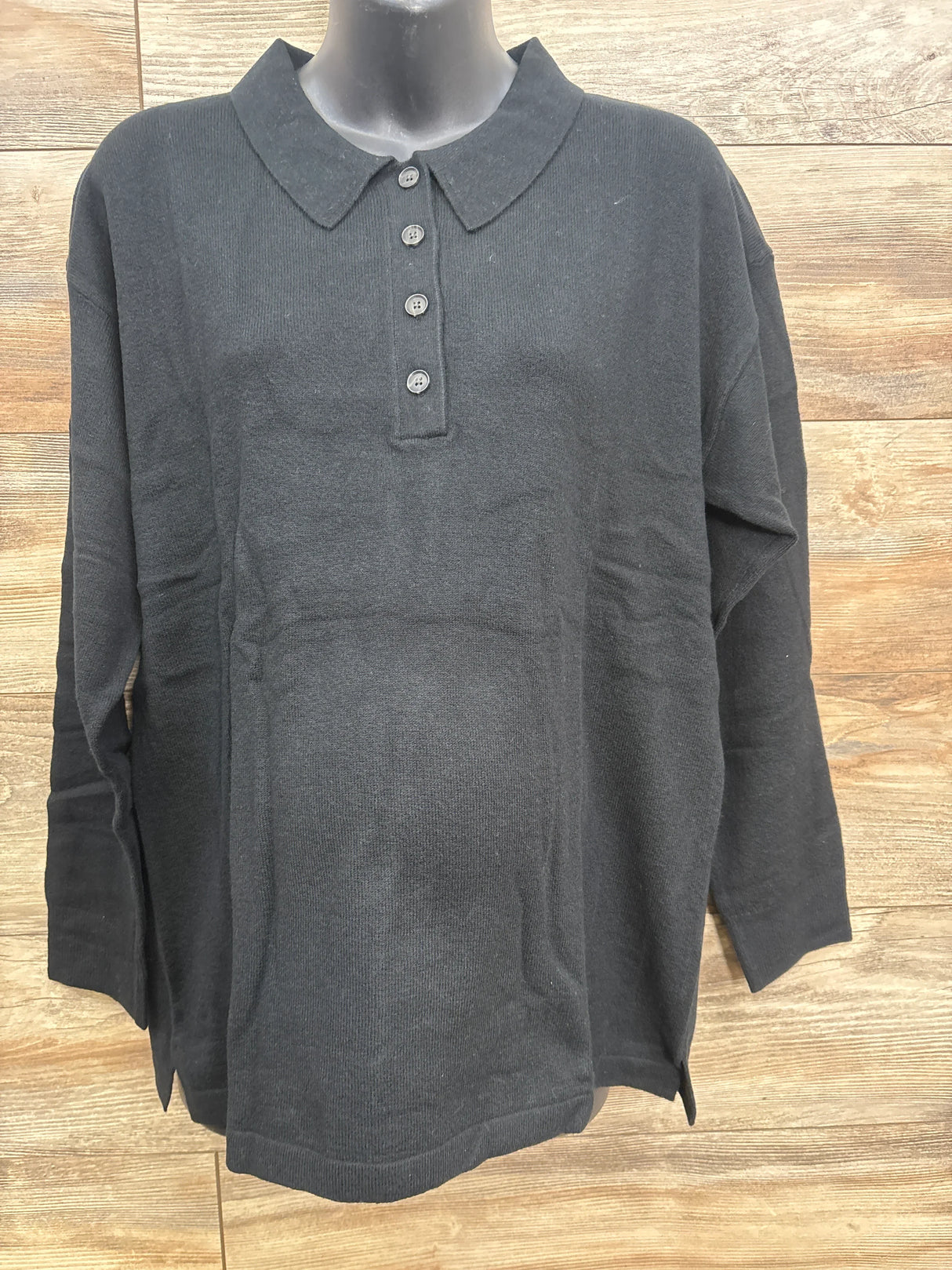 Black long sleeve children's polo shirt with four buttons displayed on mannequin against wooden background