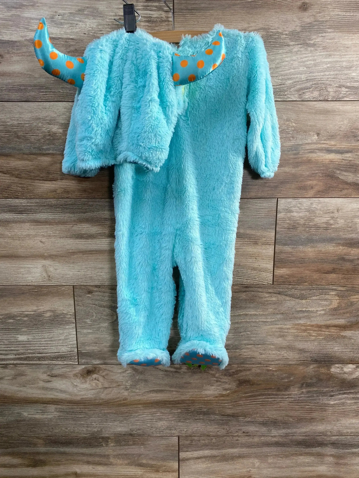 Front view of light blue furry baby monster romper size 6-12 months showcasing orange polka-dot horns and sole grips on wood floor background