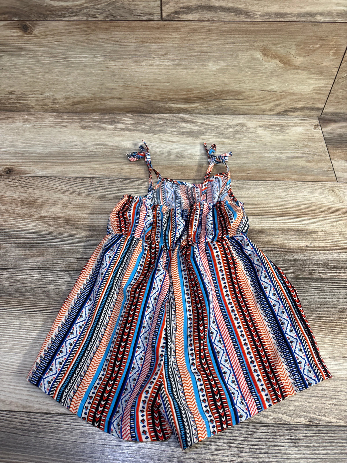 Flat lay of patterned tank shortie romper showcasing tie shoulder straps and elastic waist on wood floor